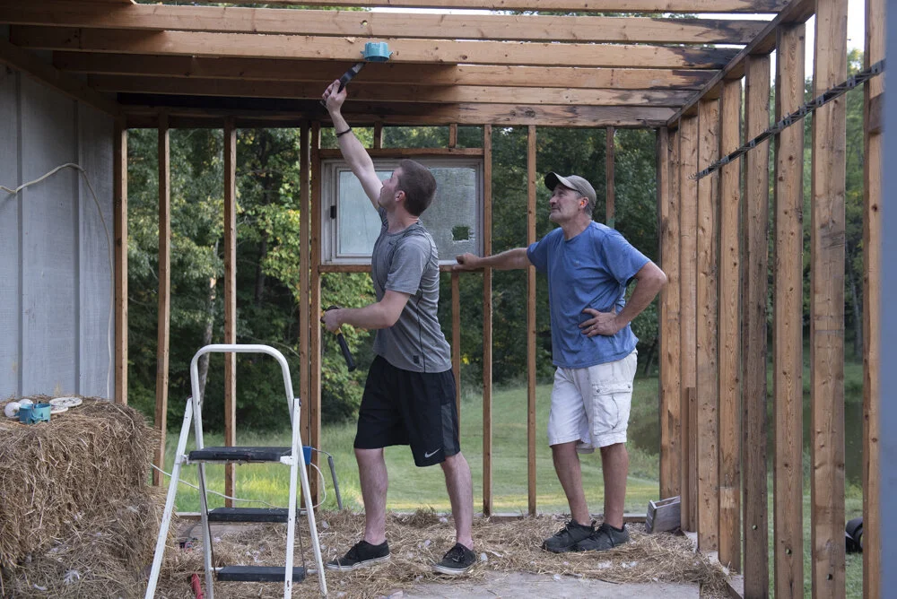   Greg and Marlene’s son Brandon, left, helps his father tear down part of the shed in the backyard so that they can rebuild it as a home for the geese.  