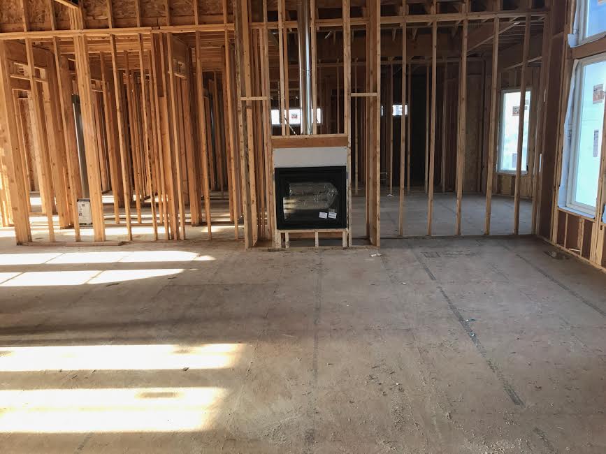 Standing at the back of the living room looking towards fireplace wall. The fireplace will be gray colored stone floor to ceiling. There will also be built in shelves on either side of the fireplace.