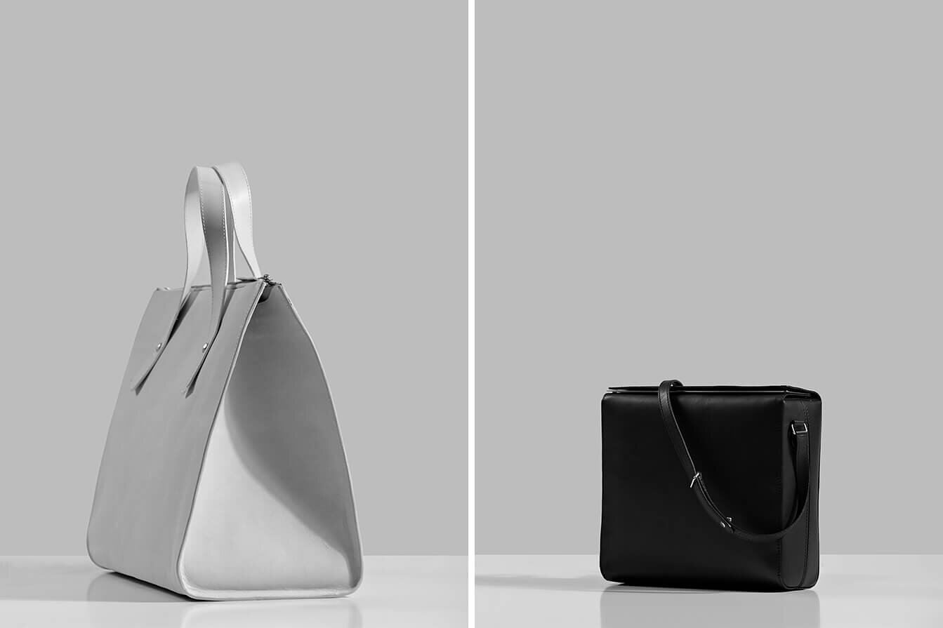 Black and white leather bags on reflective white shelf. 