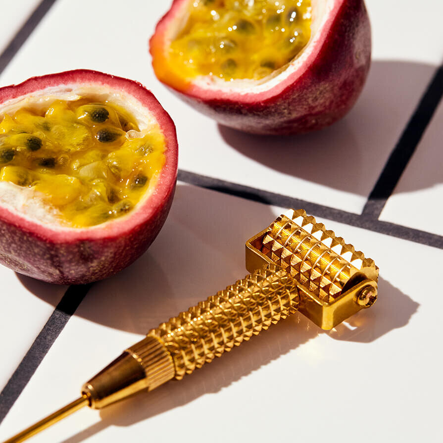 Facegym gold roller with fruit on white tiles.