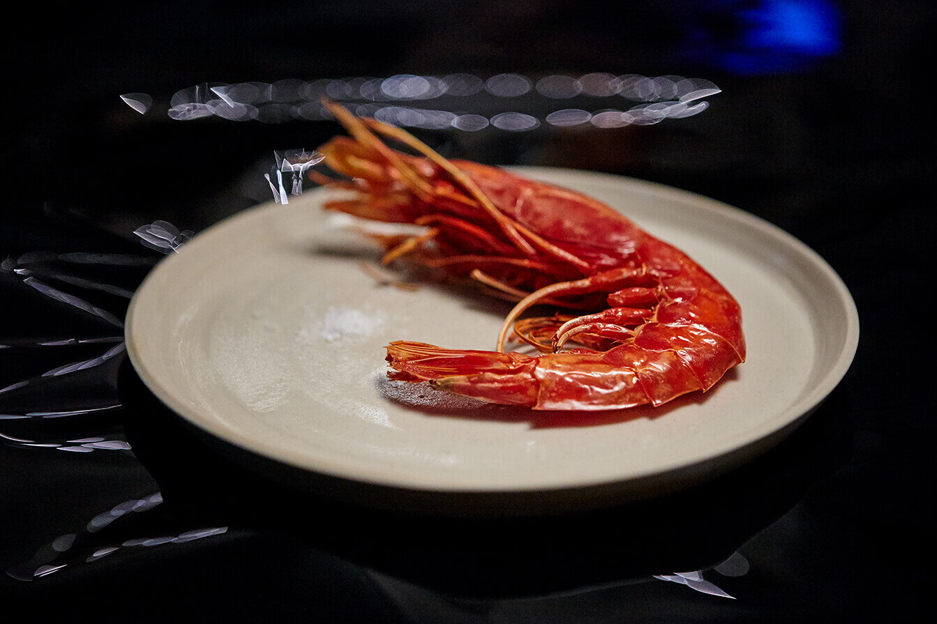 Shrimp on white plate with blue and black background.