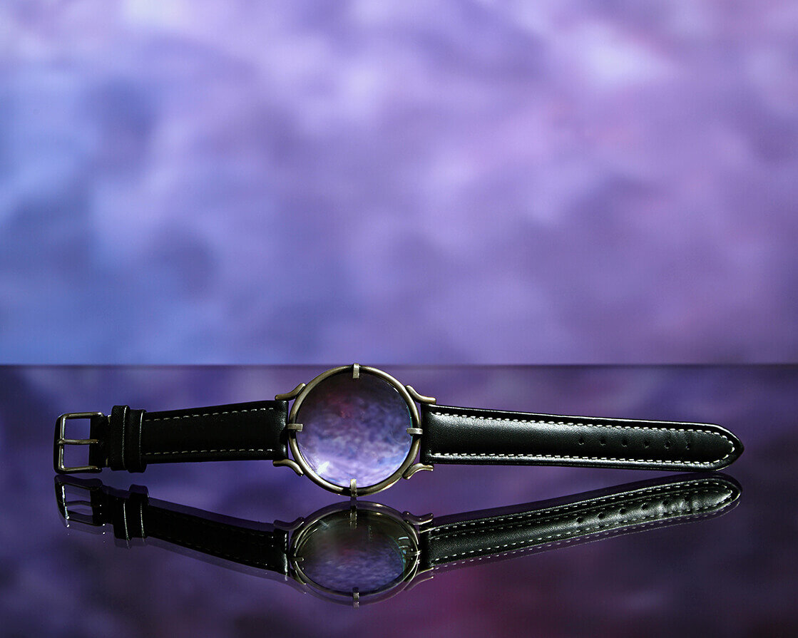Watch like bracelet on black glass shelf. Mottled purple and blue background.