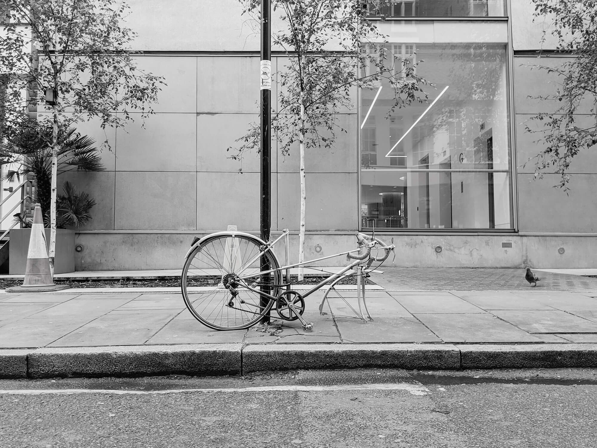 De parted bike resting on lamp post. Front wheel missing in front of London office. 