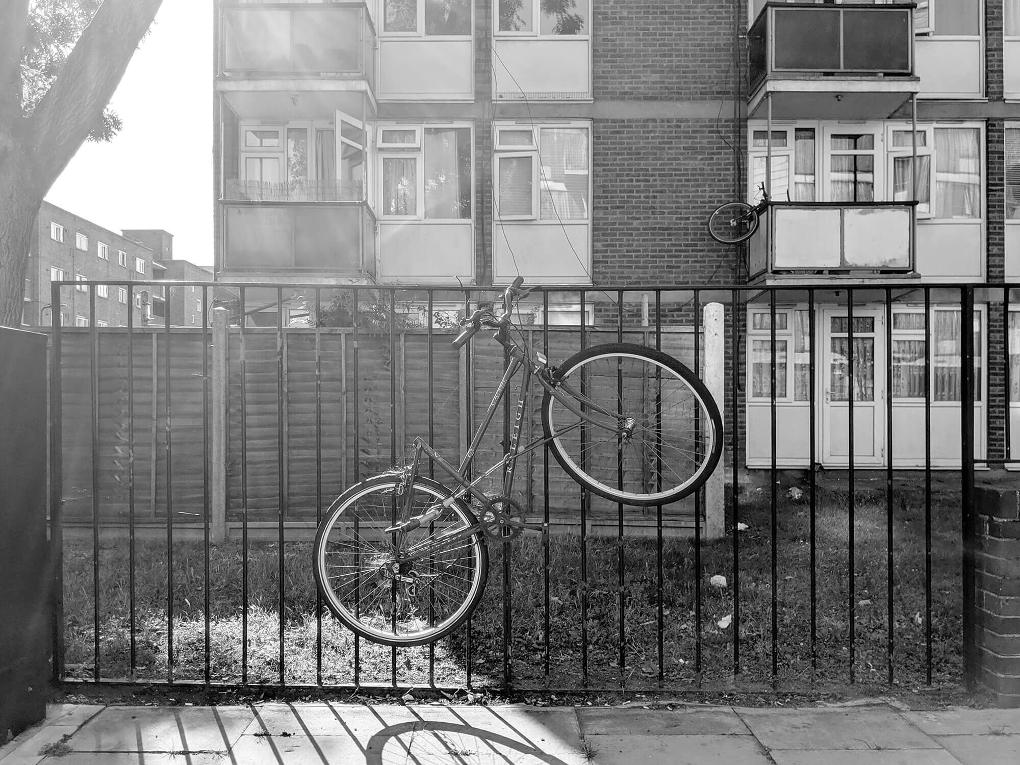 Bike chained on metal fence, with sun shining from behind.