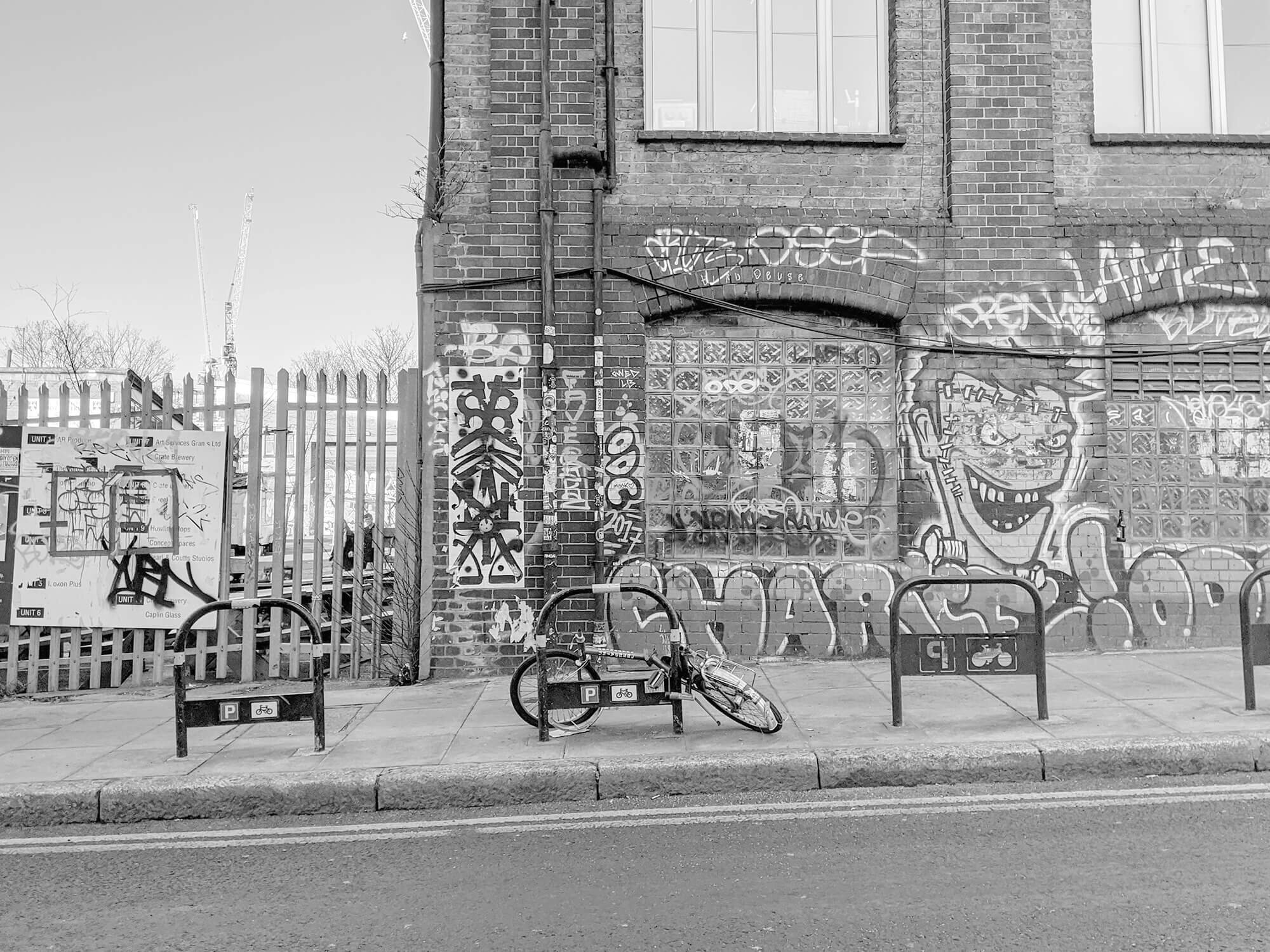 Black and white. Bicycle leaning on frame, in front of graffitied building.