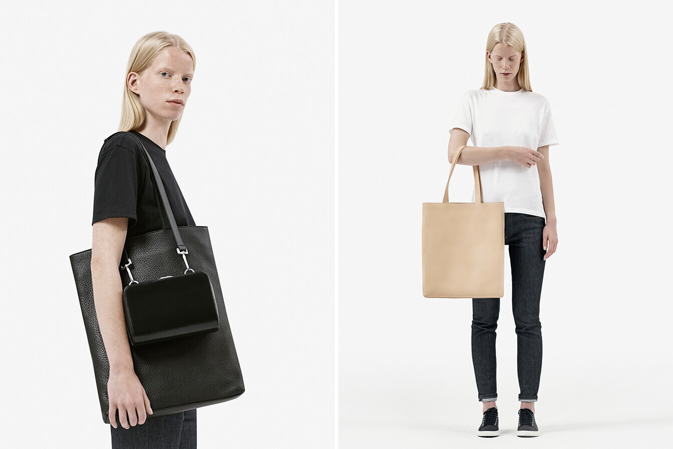 Female model stands on white background holding leather shoulder and tote bags.