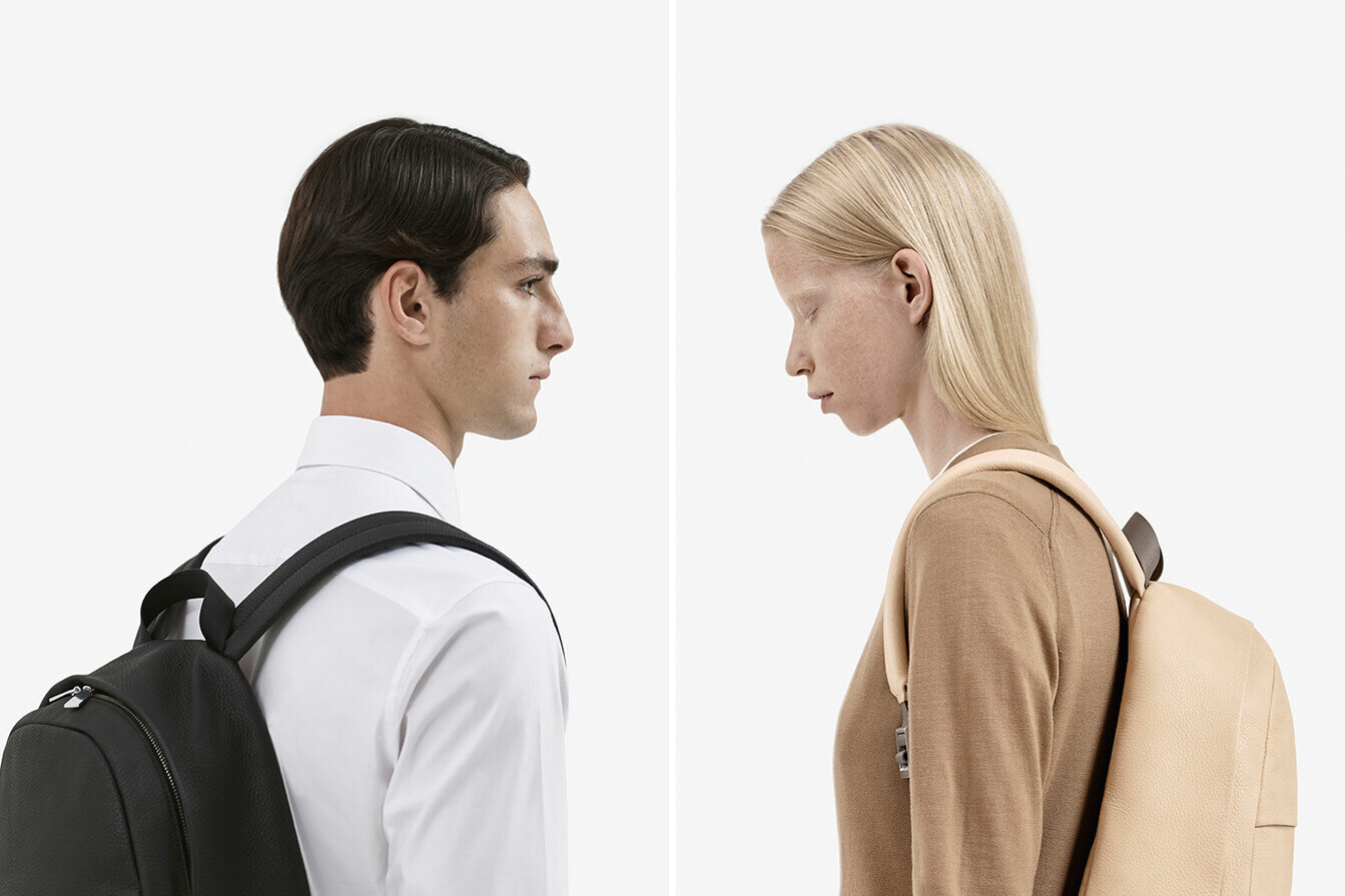 Male and female models facing each other wearing leather Silent Goods backpacks.