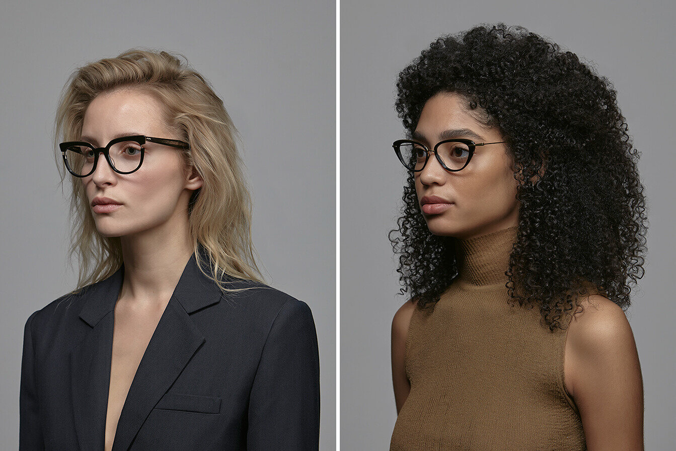 Two women modelling eyewear on a grey background. Looking off camera.