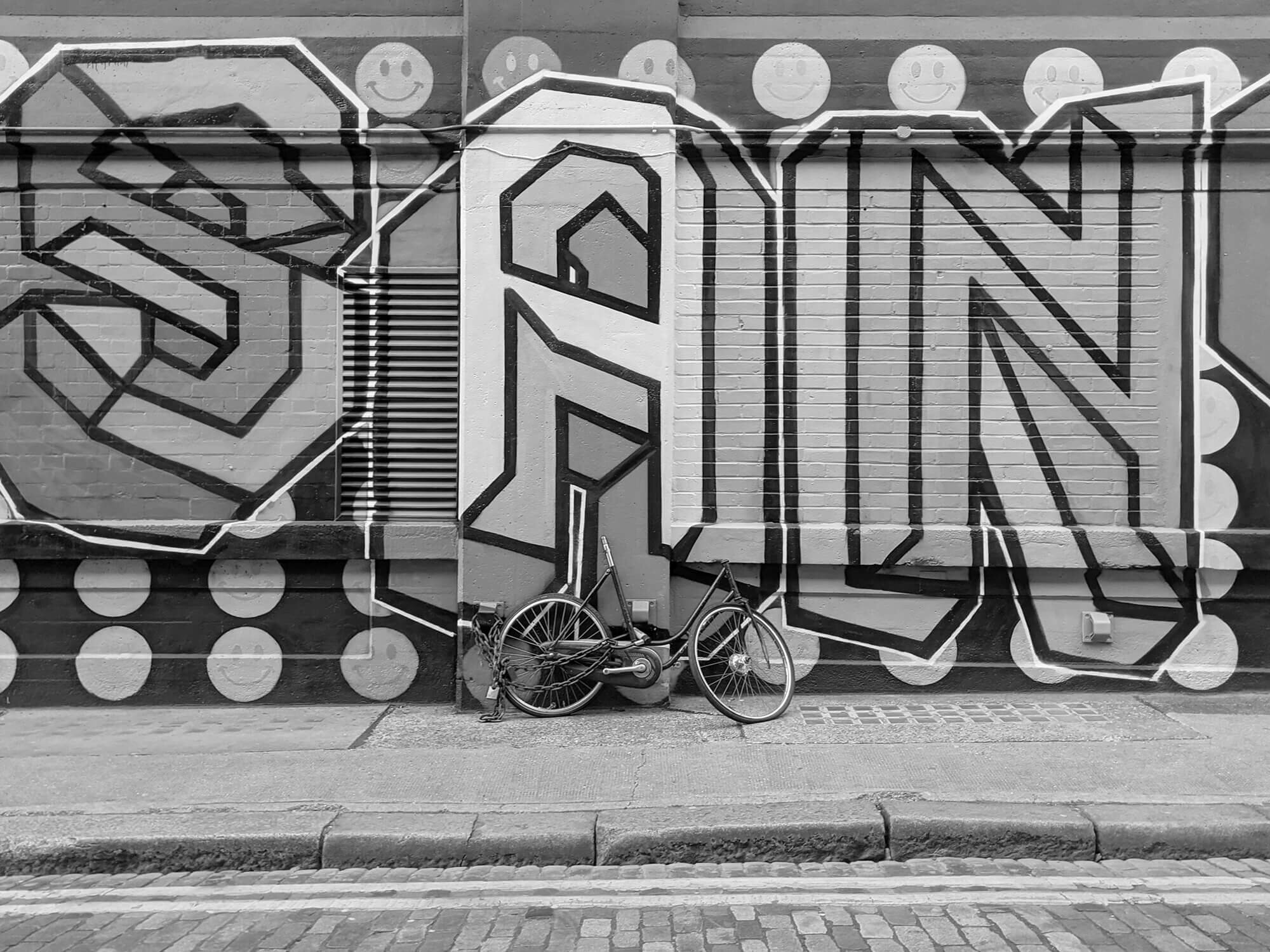 Abandoned bike in front of graffiti wall.