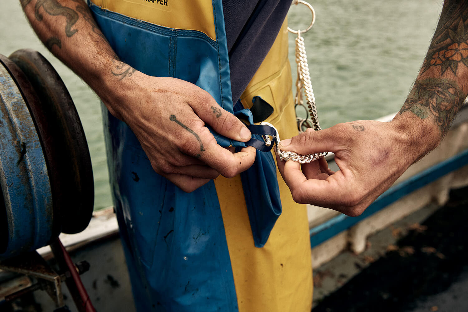 Fisherman fastening clasp on keyring. Stood on boat wearing blue and yellow waders.