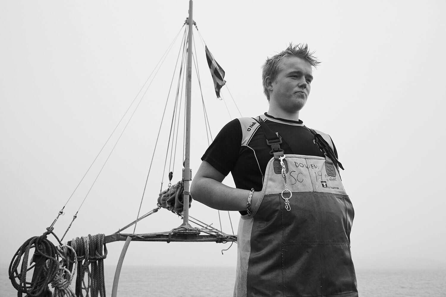 black and white photo of fisherman stood on deck wearing his waders and silver keyring