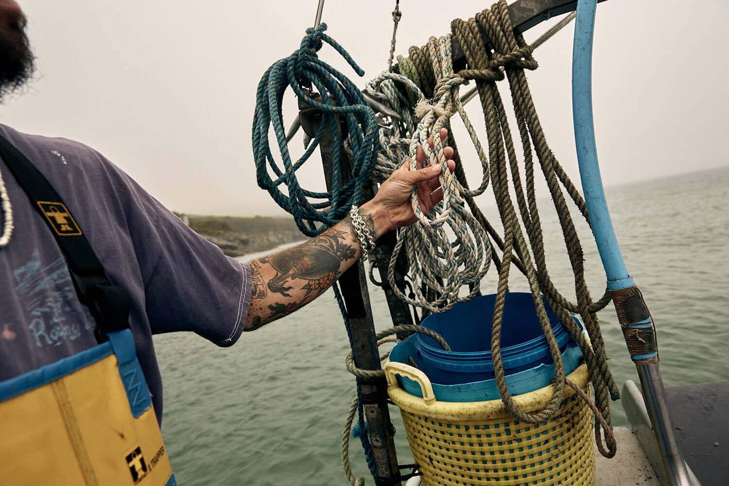colour photo of fisherman's tattooed arm holding ropes on a boat. 