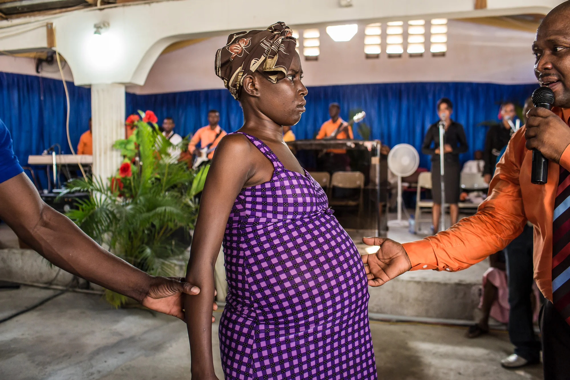 Televangelist Marcorel Zidor, right, attempts to cure a woman of an unspecified medical ailment (she is not pregnant) at L'Eglise Evangelique Piscine de Bethesda in its temporary home on Saturday, December 20, 2014 in Port-au-Prince, Haiti. Pastor Zidor attracts a large audience with his emotional services and miracle medical cures of dubious theraputic value.