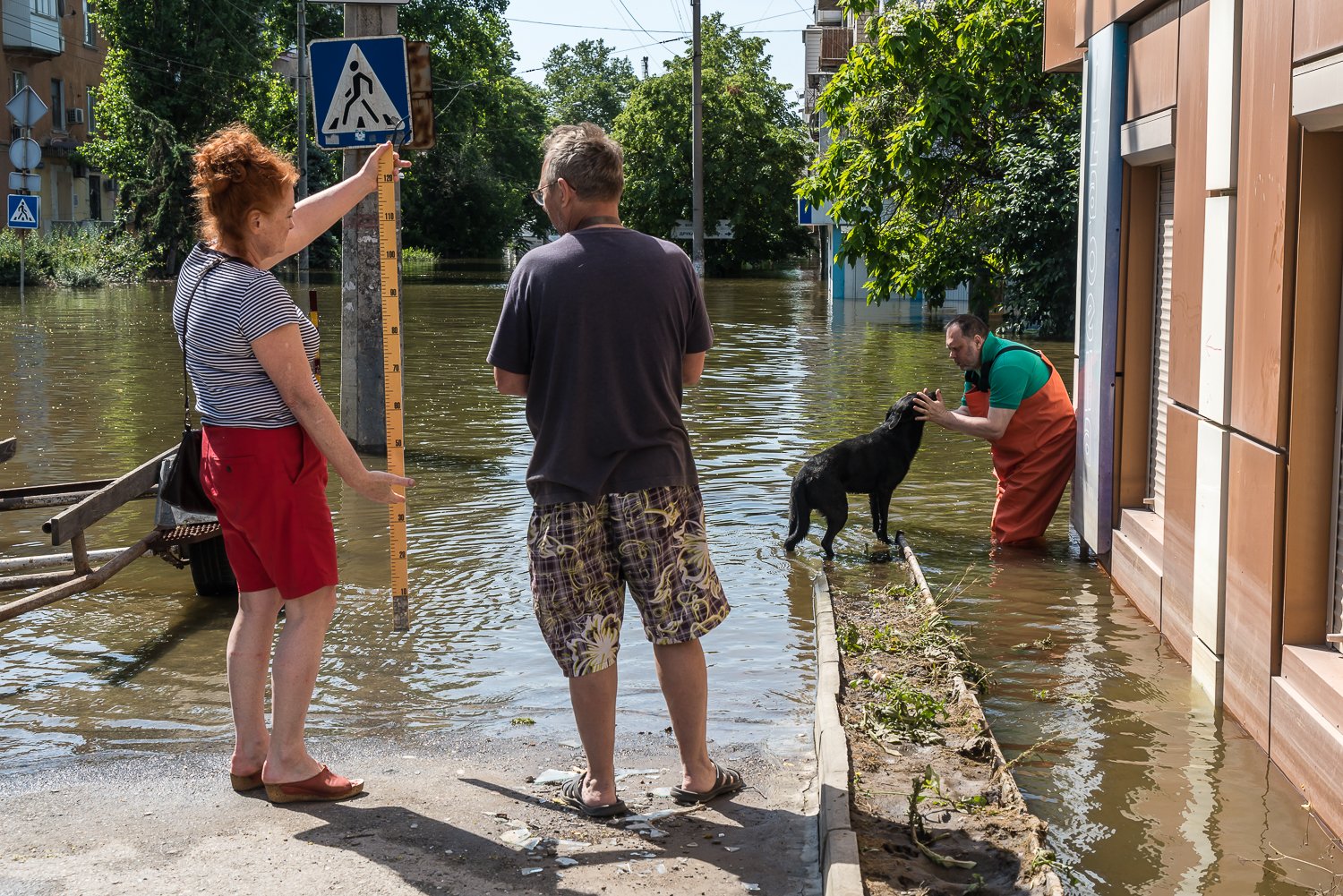  Lora Musian, left, a hydrologist from nearby Mykolaiv oblast, and volunteer Oleh Barkarneko, right, measure water levels in the city and pet a stray dog after the destruction of the hydroelectric dam at Nova Kakhovka flooded downstream communities o