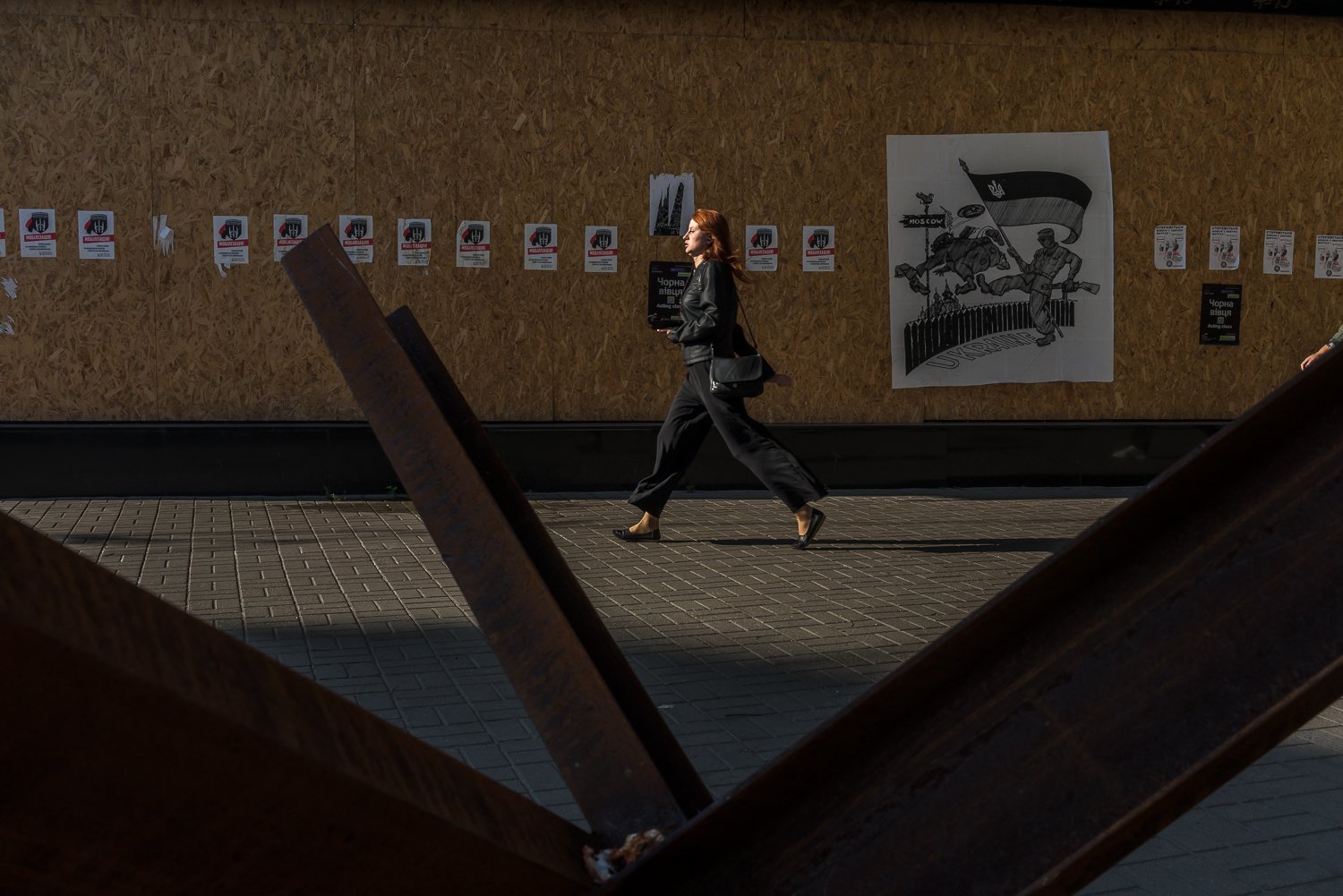  An early-morning commuter walks past a hedgehog tank trap and a patriotic poster on Friday, September 2, 2022 in Kyiv, Ukraine. 