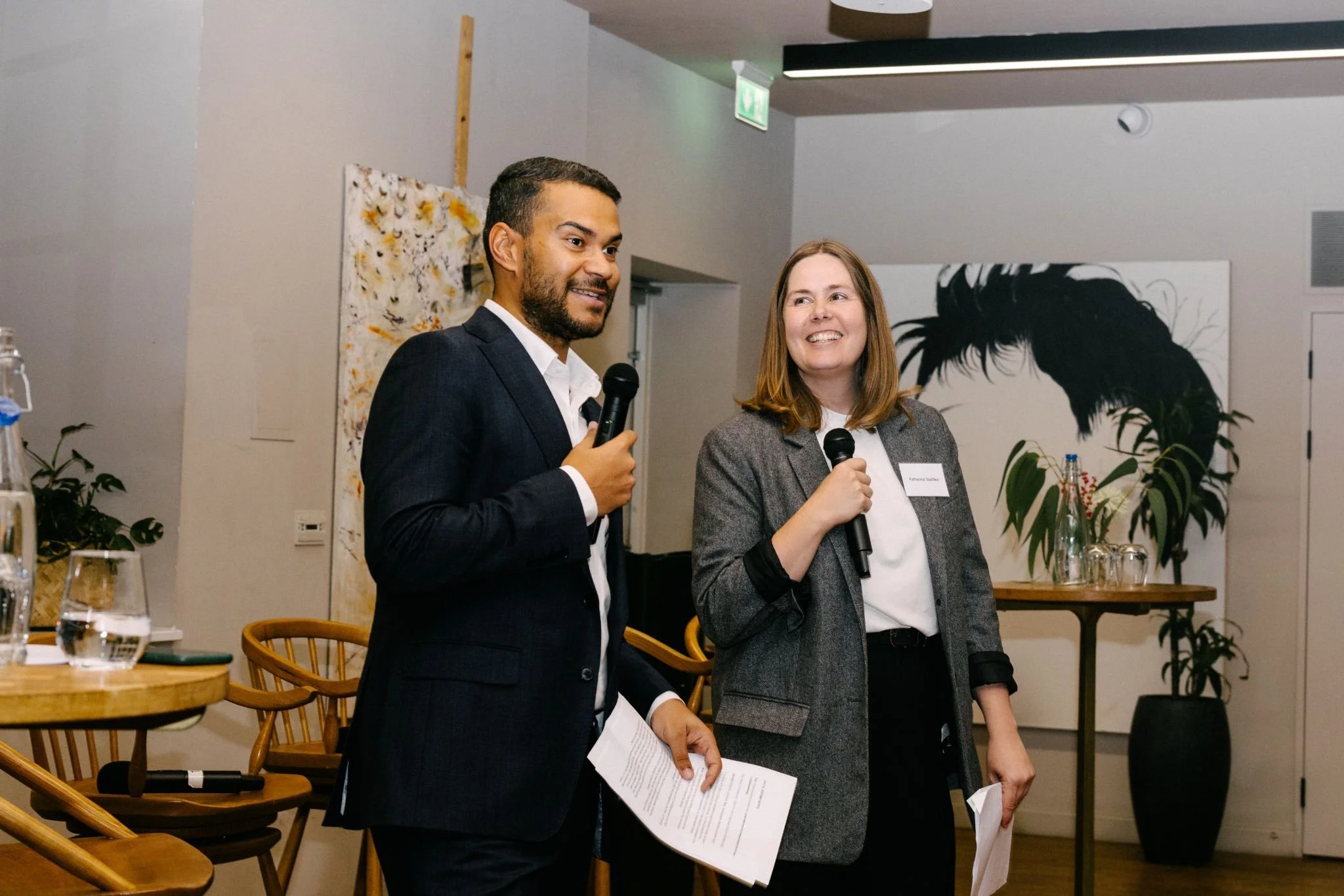 Kat with a colleague, holding a mic and speaking to a room