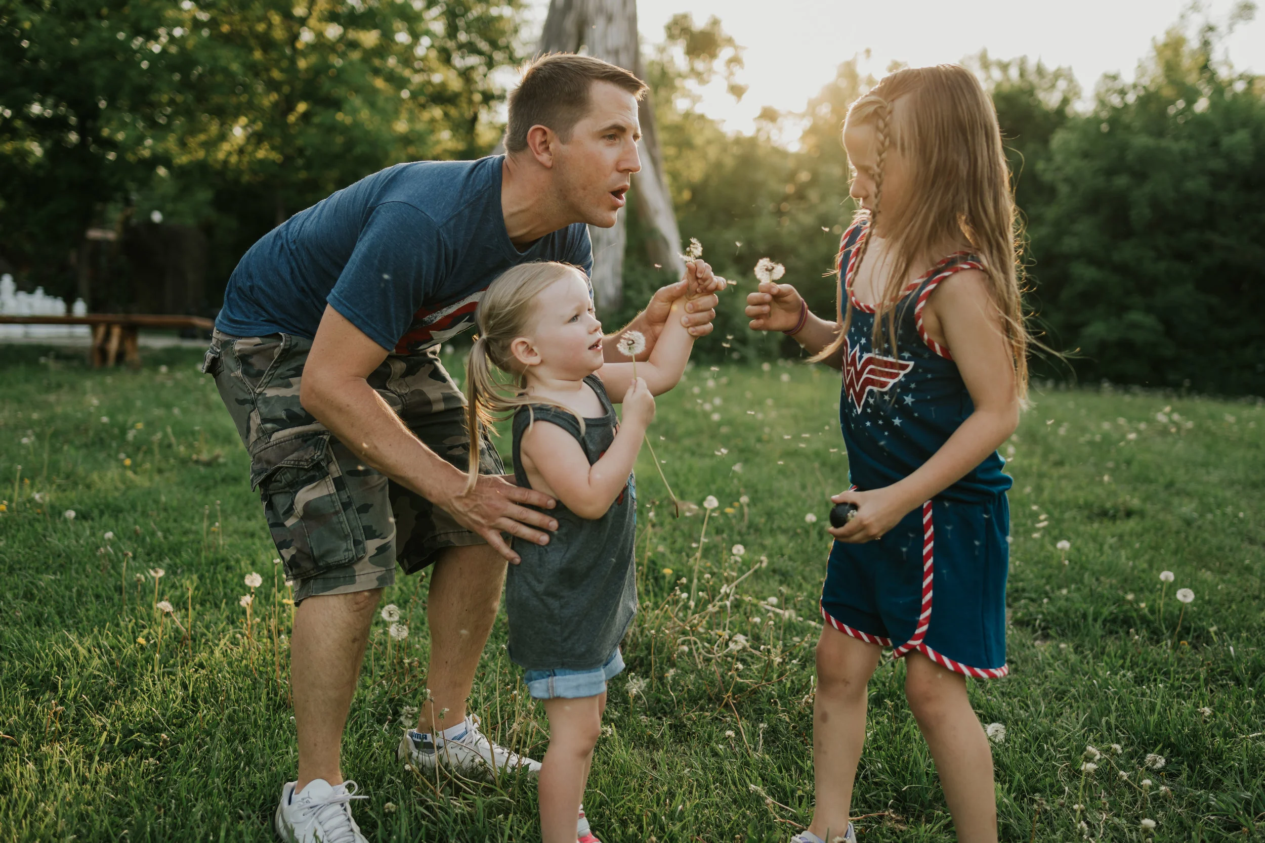 Daddy and two daughters blowing dandelions in the sun light - Minnetonka Family Photographer