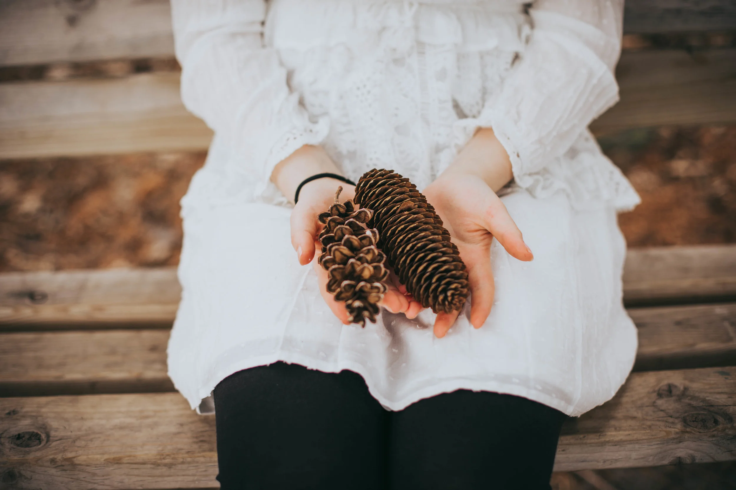 girl in a white dress holding pinecones while sitting on a bench