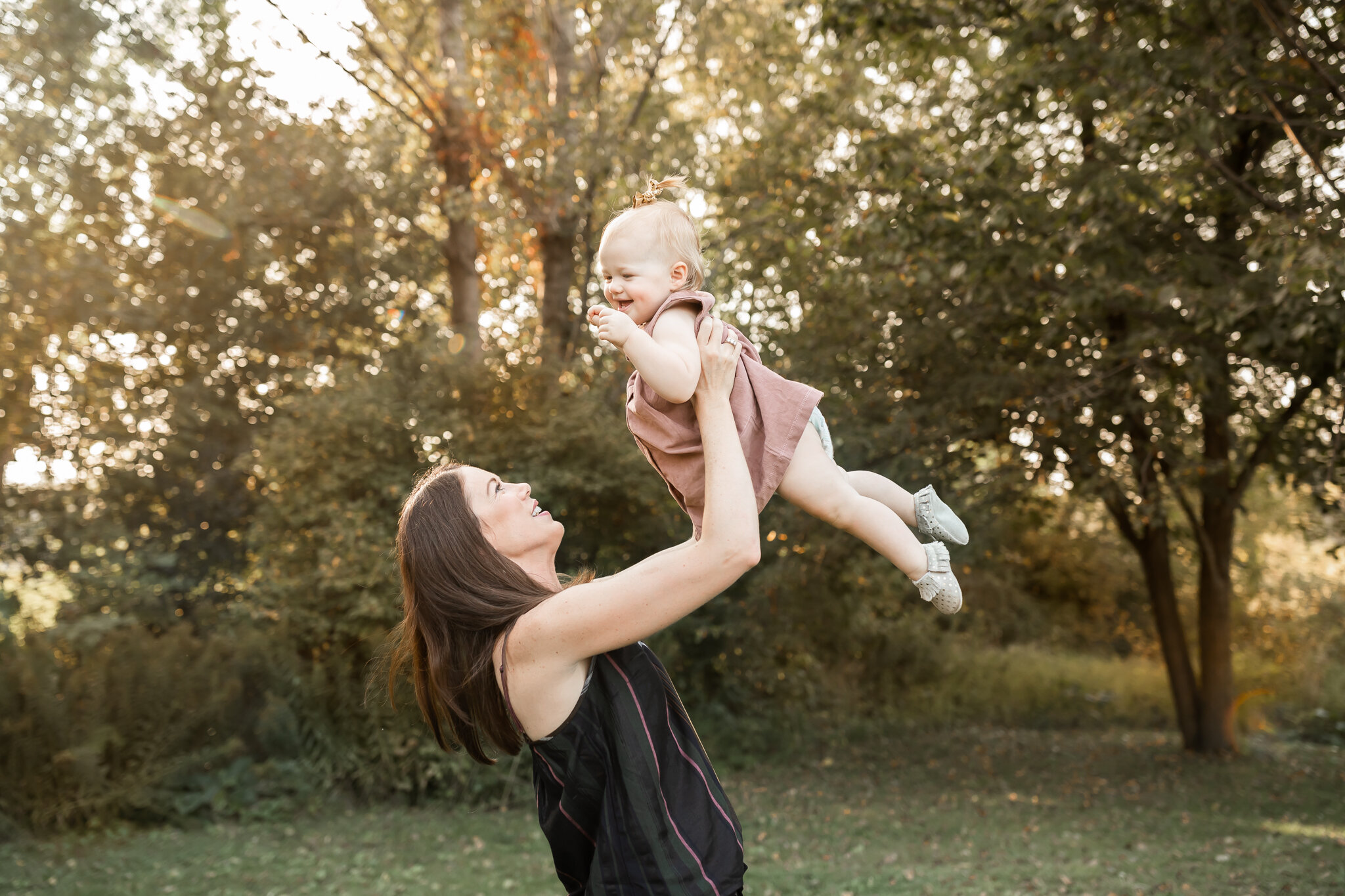woman in black shirt holding up her baby girl laughing - AMG Photography