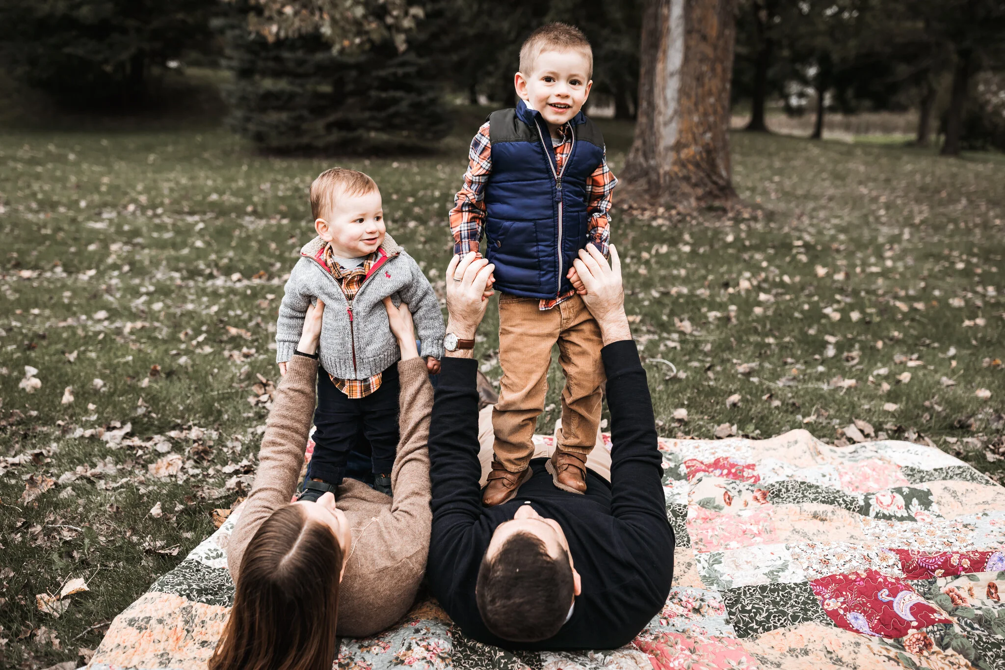 two brothers standing on top of their mom and dad in the fall leaves | AMG Photography