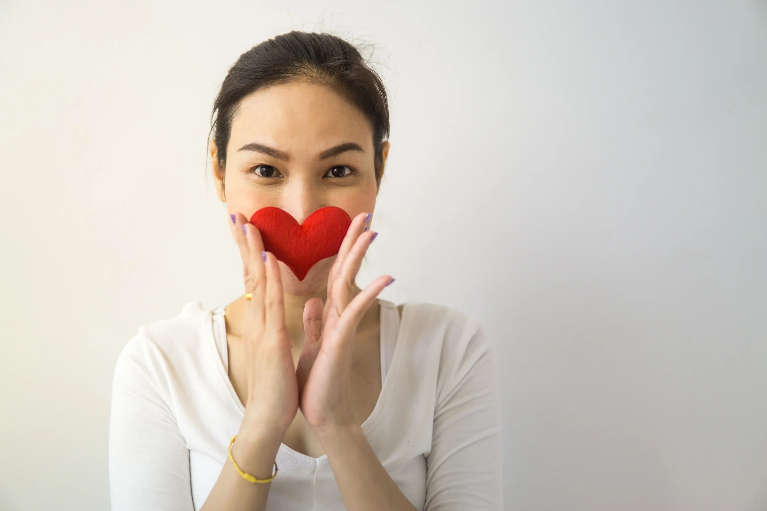 A woman holding a red paper cutout of a heart in front of her face