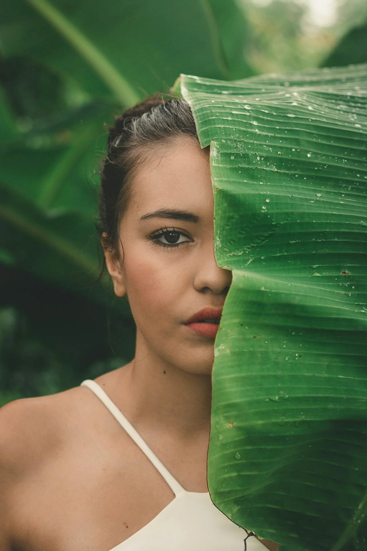 Serene woman in nature with tropical leaf covering half her face