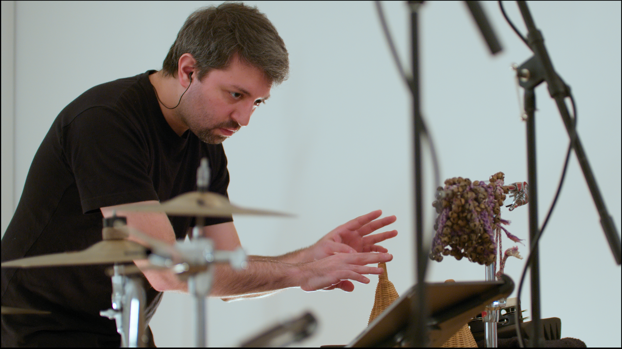 2. A close-up image of a percussionist playing a caxixi with their fingertips. The caxixi is a brown, shaker-like instrument, and is placed on a foam pad.