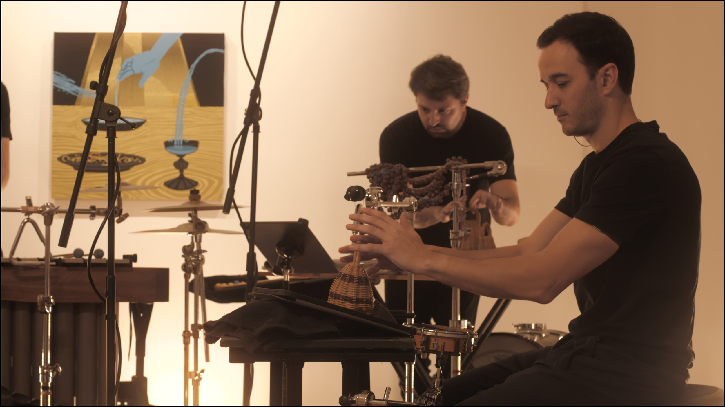 11. A close-up image of two percussionists playing caxixis with their fingertips. The caxixis are a brown, shaker-like instrument, and is placed on a foam pad.