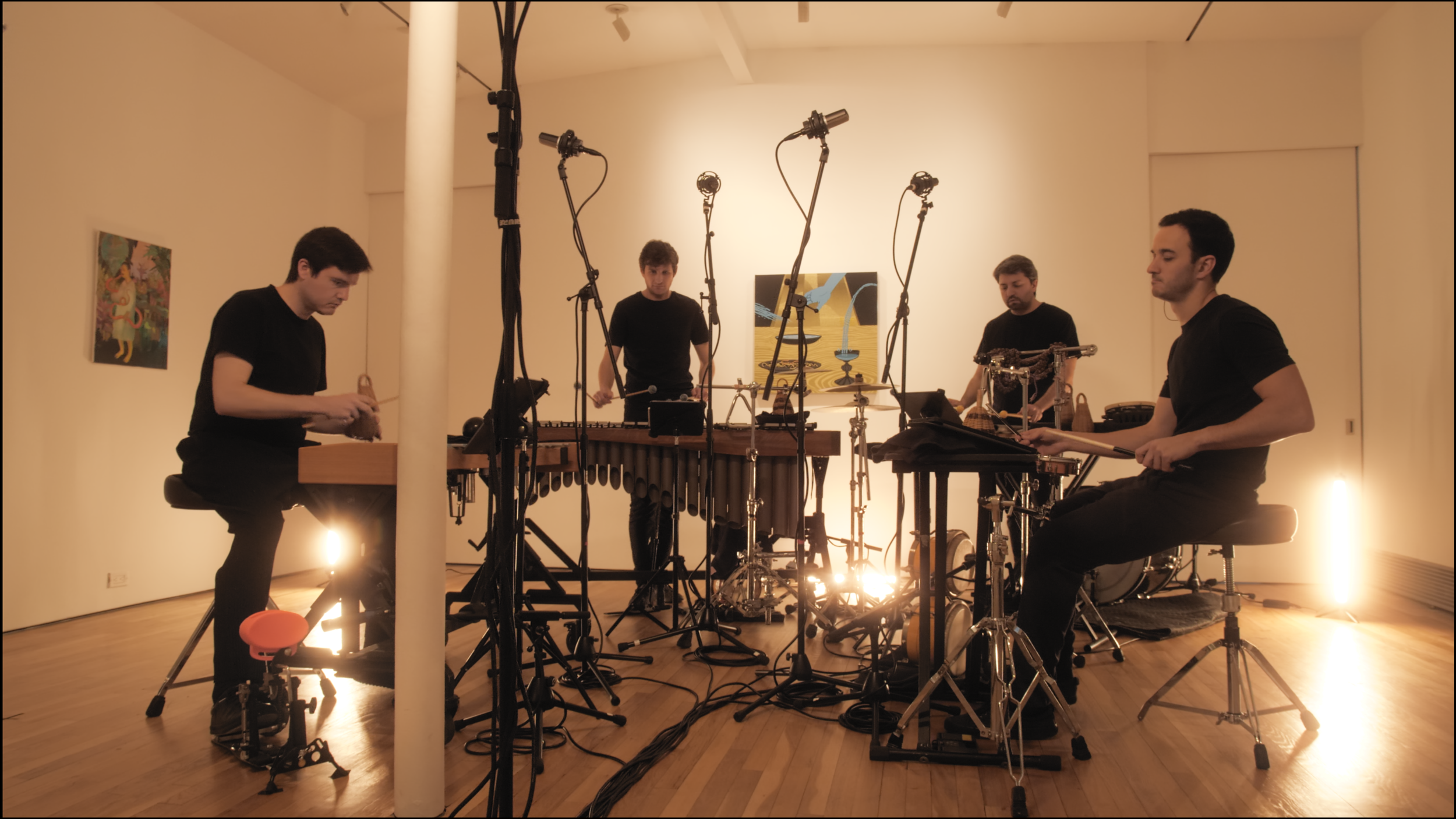12. An image of four percussionists playing in a semi-circle format, seated and standing, playing various instruments such as a vibraphone, caxixi, and handclaps.