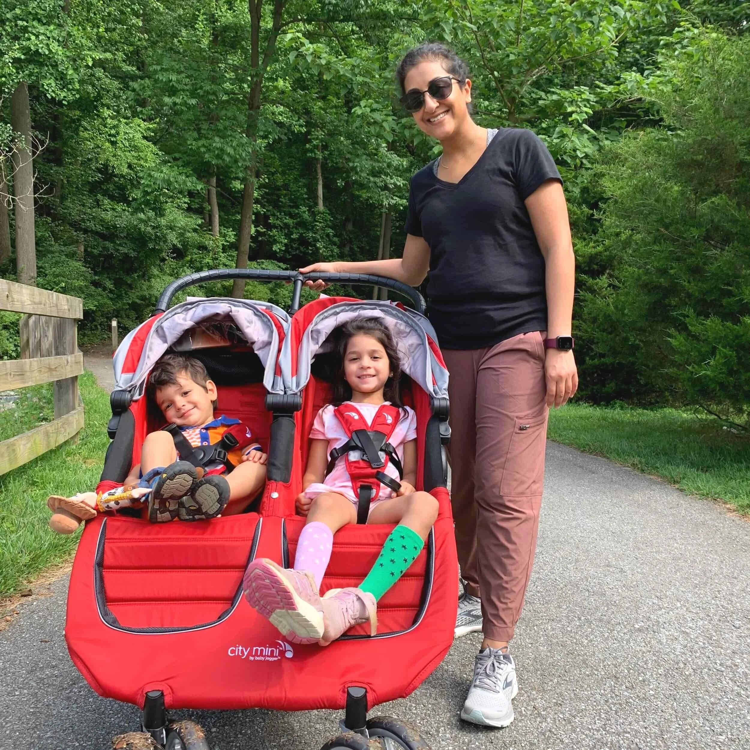 mom standing next to her red double stroller out for a walk with her two kids
