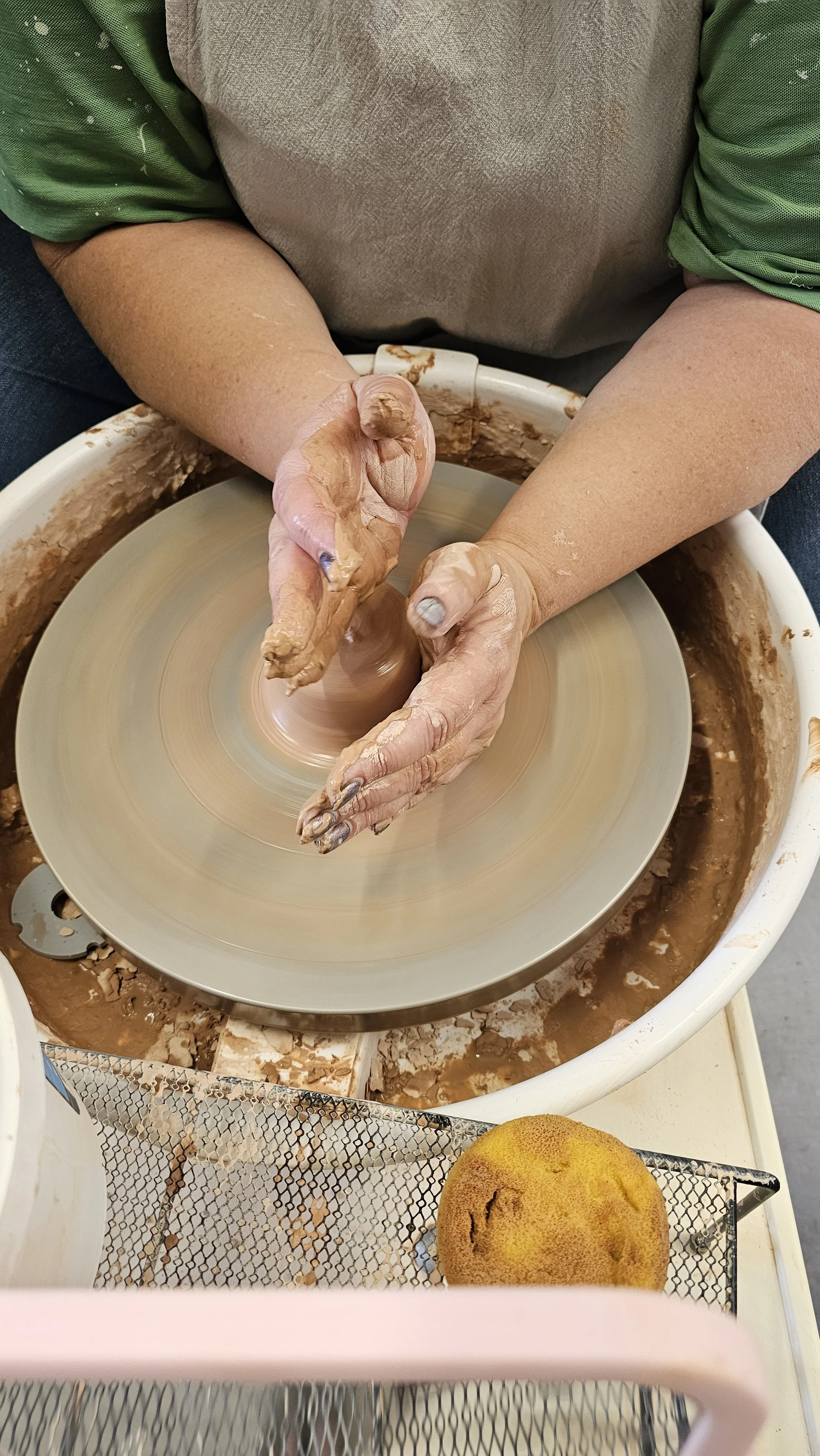 A beginner learning to centre clay, focused and steady at the wheel