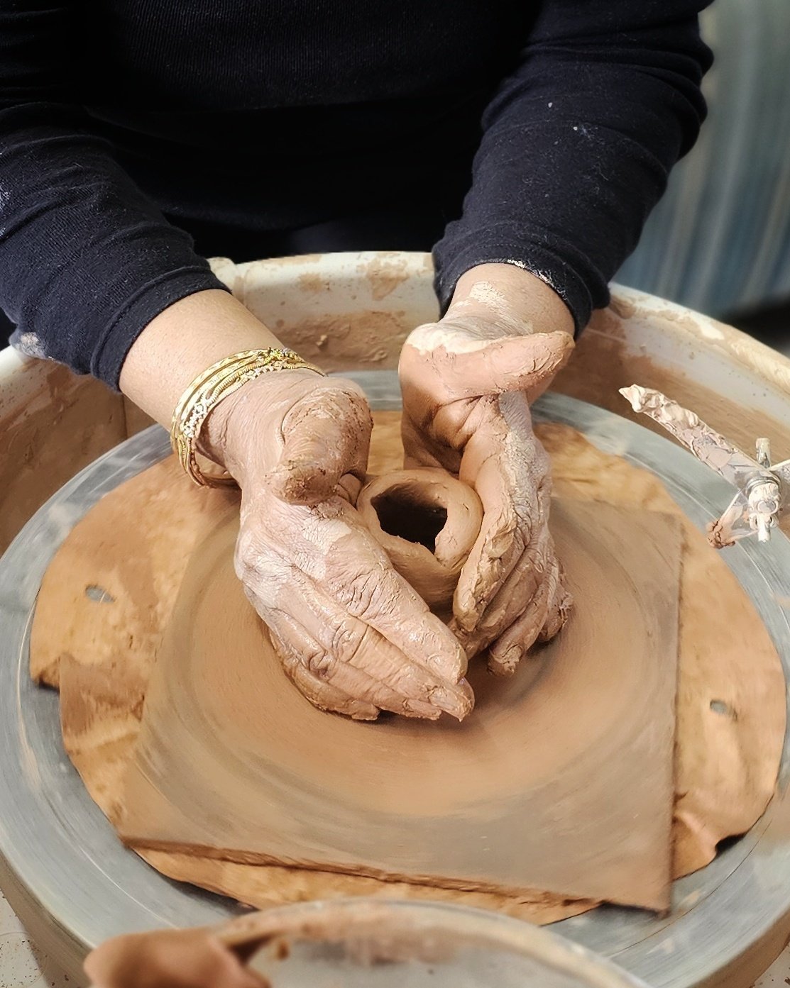 Hands working with clay as it spins on a pottery wheel in a small studio setting