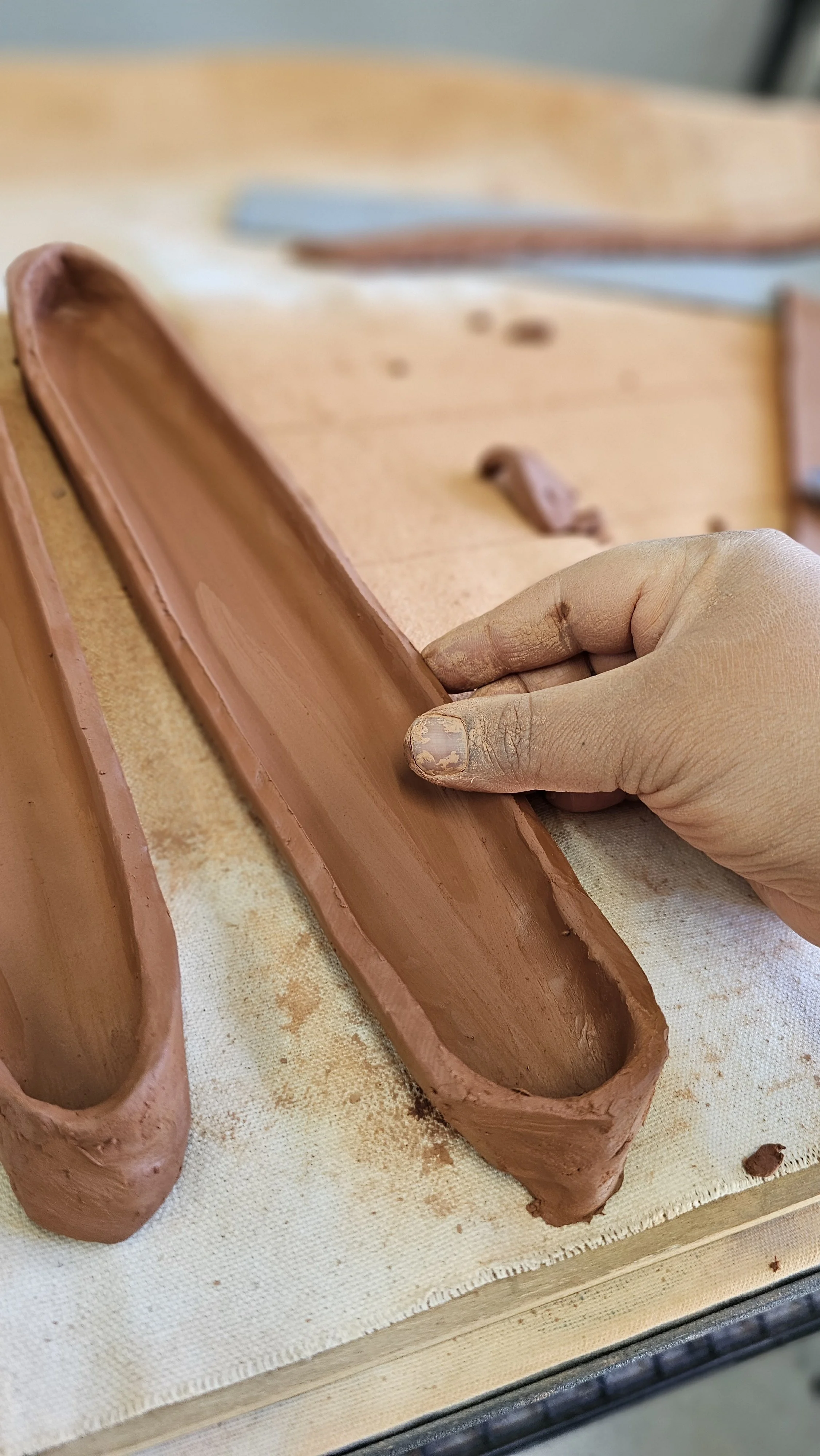 Unfinished ceramic mug with a heart and the word 'DAD' engraved on it, displayed on a wooden table with other similar pottery in the background.