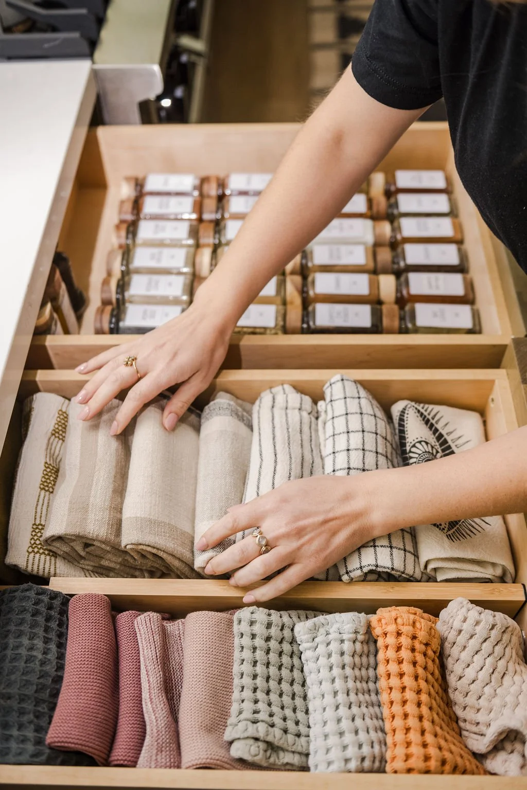 Hands neatly folding dish towels into an organized kitchen drawer using a functional vertical filing system.