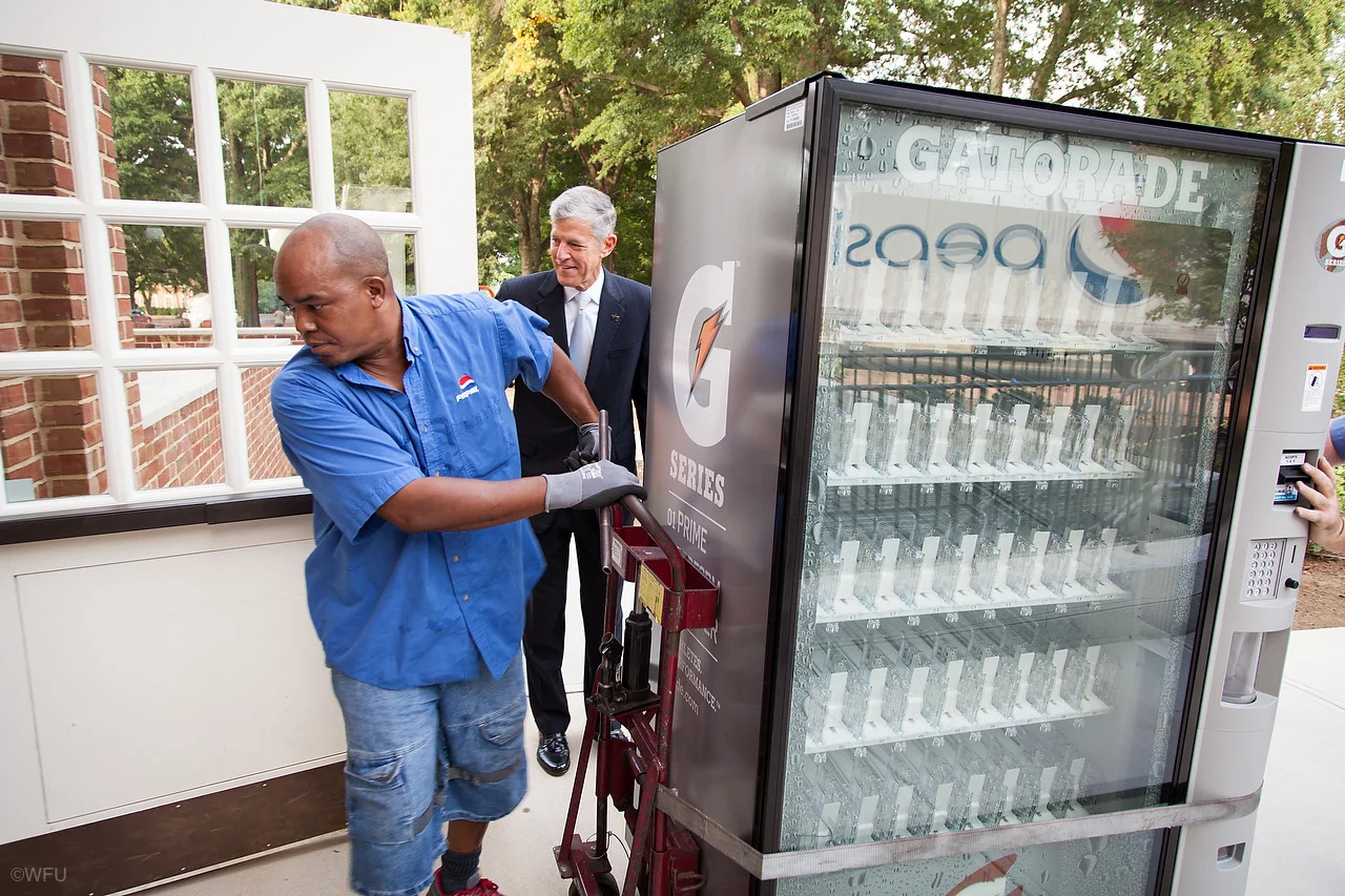Caption: Steve Reinemund, former CEO of Pepsico and now the dean of the Wake Forest business school, holds the door as two Pepsi workers install a vending machine in Farrell Hall Friday morning. Courtesy of Ken Bennett, Wake Forest University Tumblr