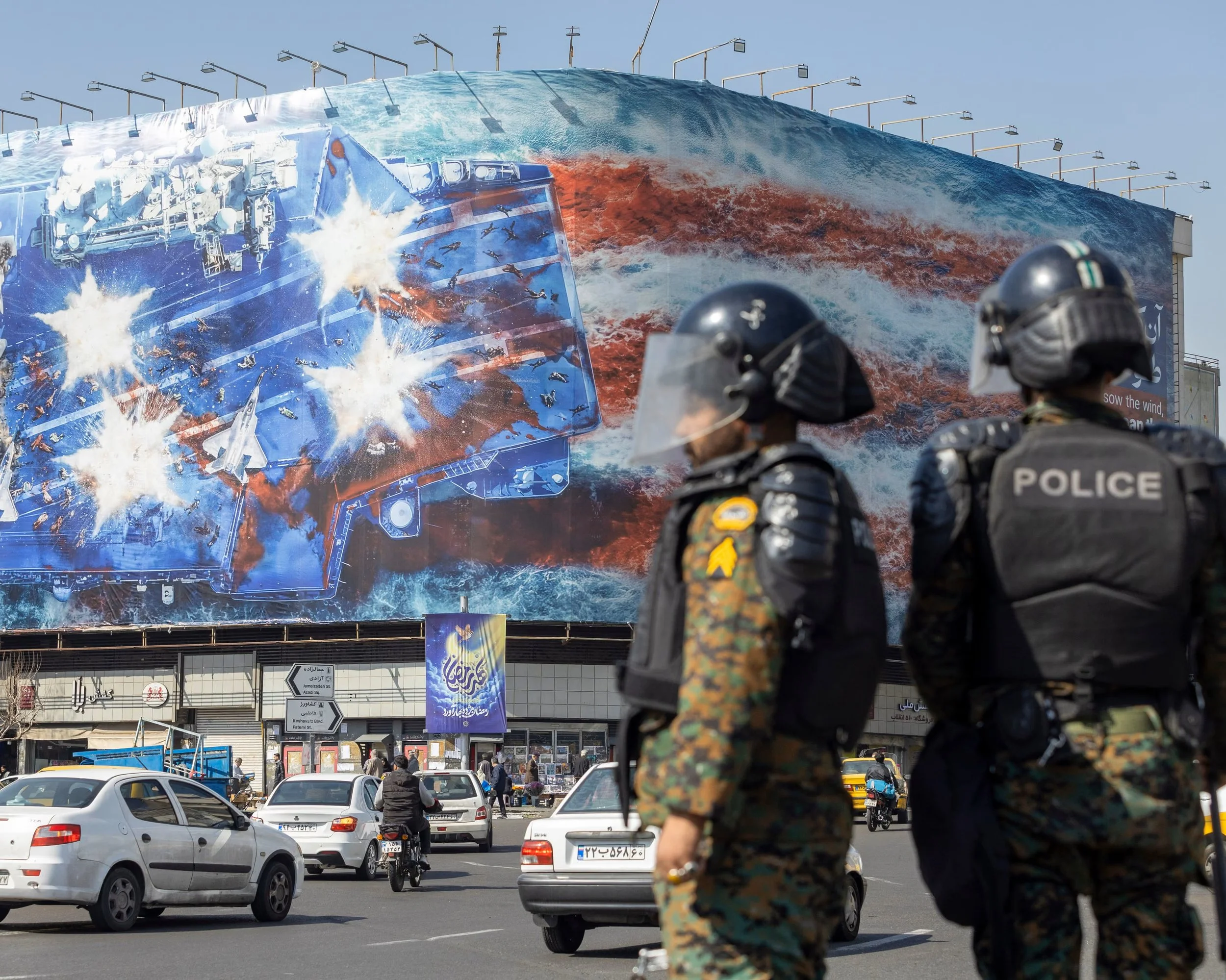 Anti-riot police in central Tehran in front of a state building covered with a billboard depicting the destruction of a US aircraft carrier.