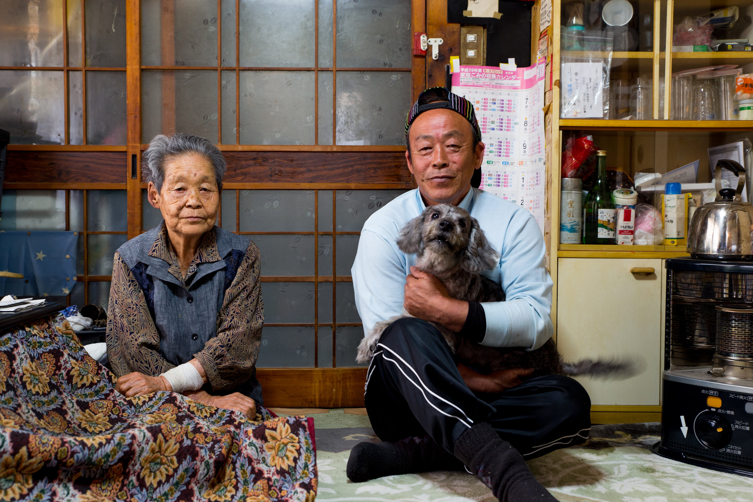 Fisherman Tomo Komatsu and his mother, Hatsui Komatsu, sit in their living room with their dog Marine. Hatsui has lived in her house in Nakoso for more than 60 years. She has other children but they have moved away. Tomo Komatsu has stayed to take c