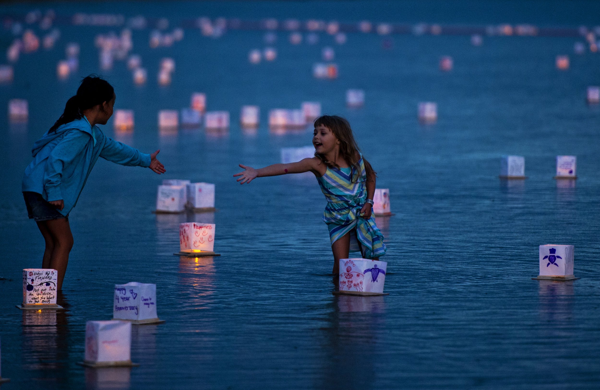  Six-year-olds Jade Padmore, left, and Parker Scott, reach towards each other as they wade in the water, surrounded by lanterns during the Colorado Springs Water Lantern Festival at Prospect Lake on Saturday, July 19, 2019. Community members were inv