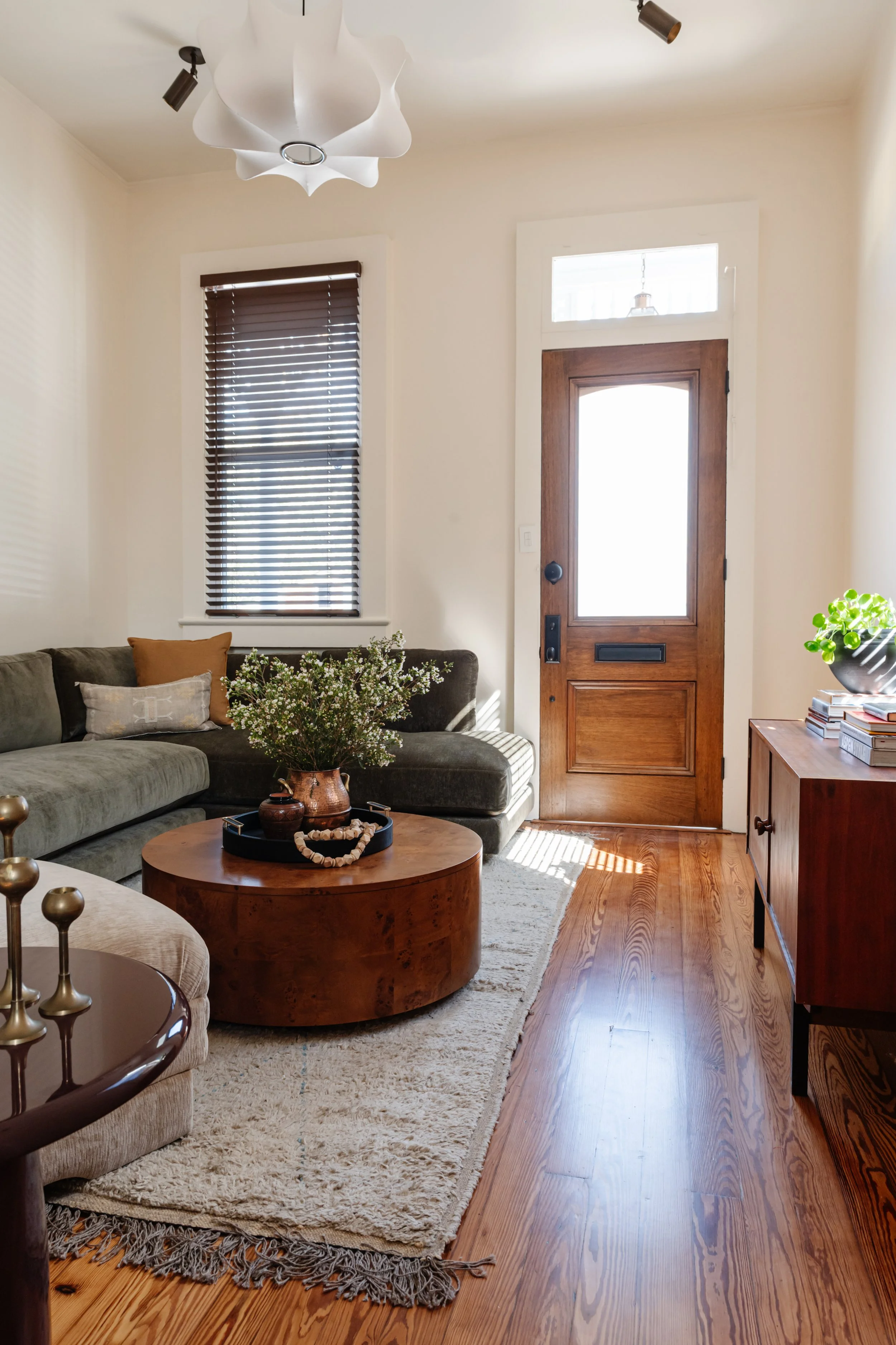 Living room: Living room with green velvet sectional and round storage coffee table in a New Orleans shotgun home