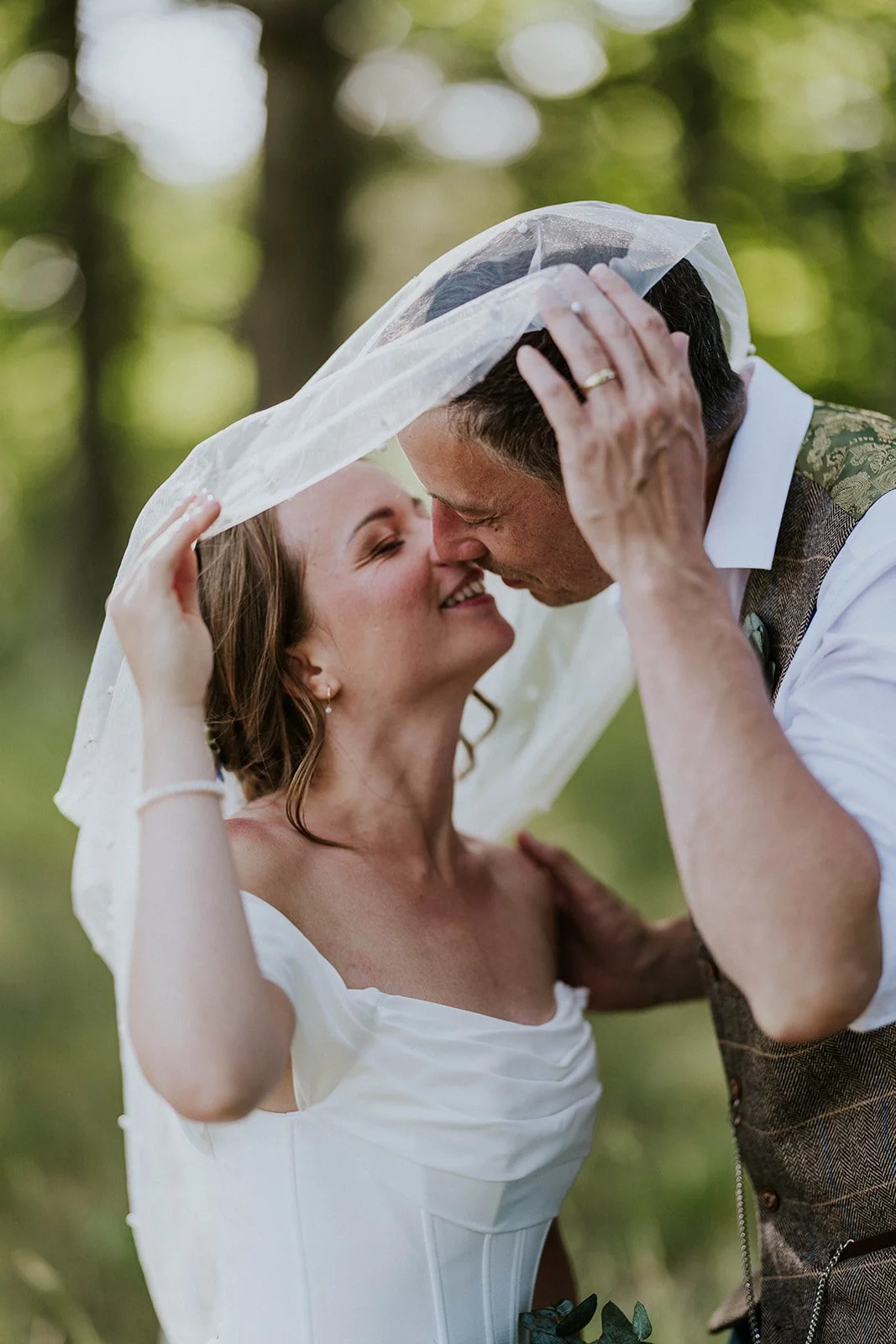 A close-up photo of the bride and groom kissing under a wind-catching bridal veil at Vesterstrand beach on Aero, with the husband's wedding ring visible.