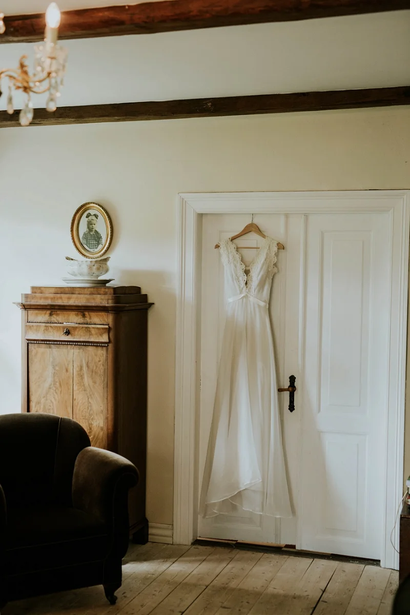 An elegant and simple wedding dress arranged in a rustic interior setting before an intimate micro-wedding ceremony in Aeroe, Denmark.