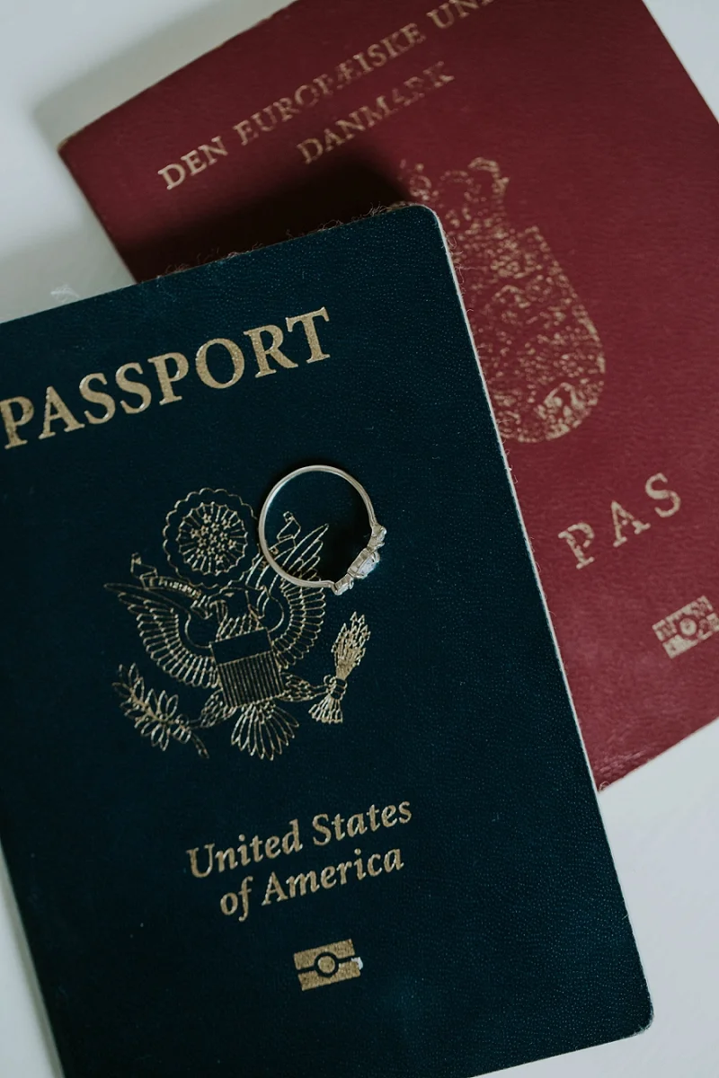 • Close-up of a diamond wedding ring resting on an international passport, illustrating the simple legal paperwork process for couples getting married in Denmark.