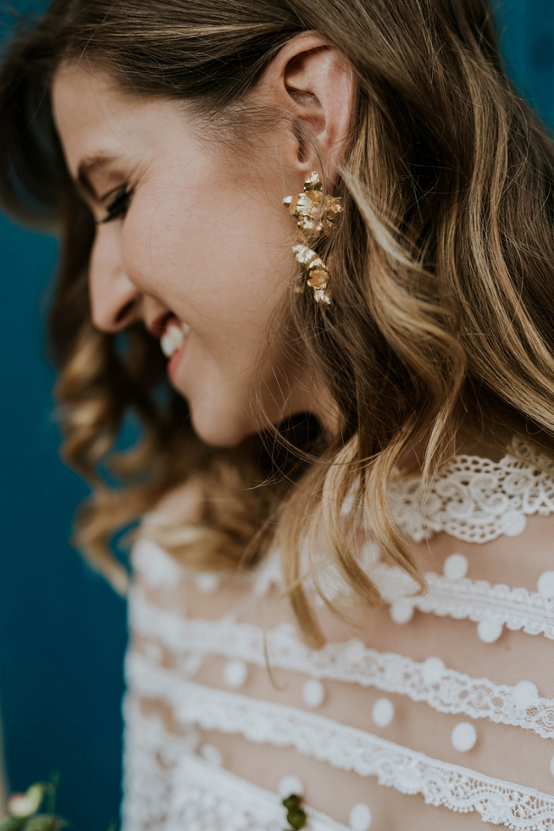 Blonde bride in profile with long wedding hair and large gold earring wearing a lace dress