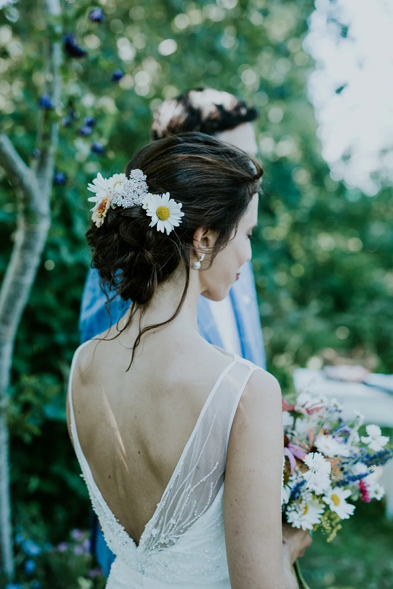 Brunette bride from behind with bridal updo with daisy flowers holding a seasonal wedding bouquet