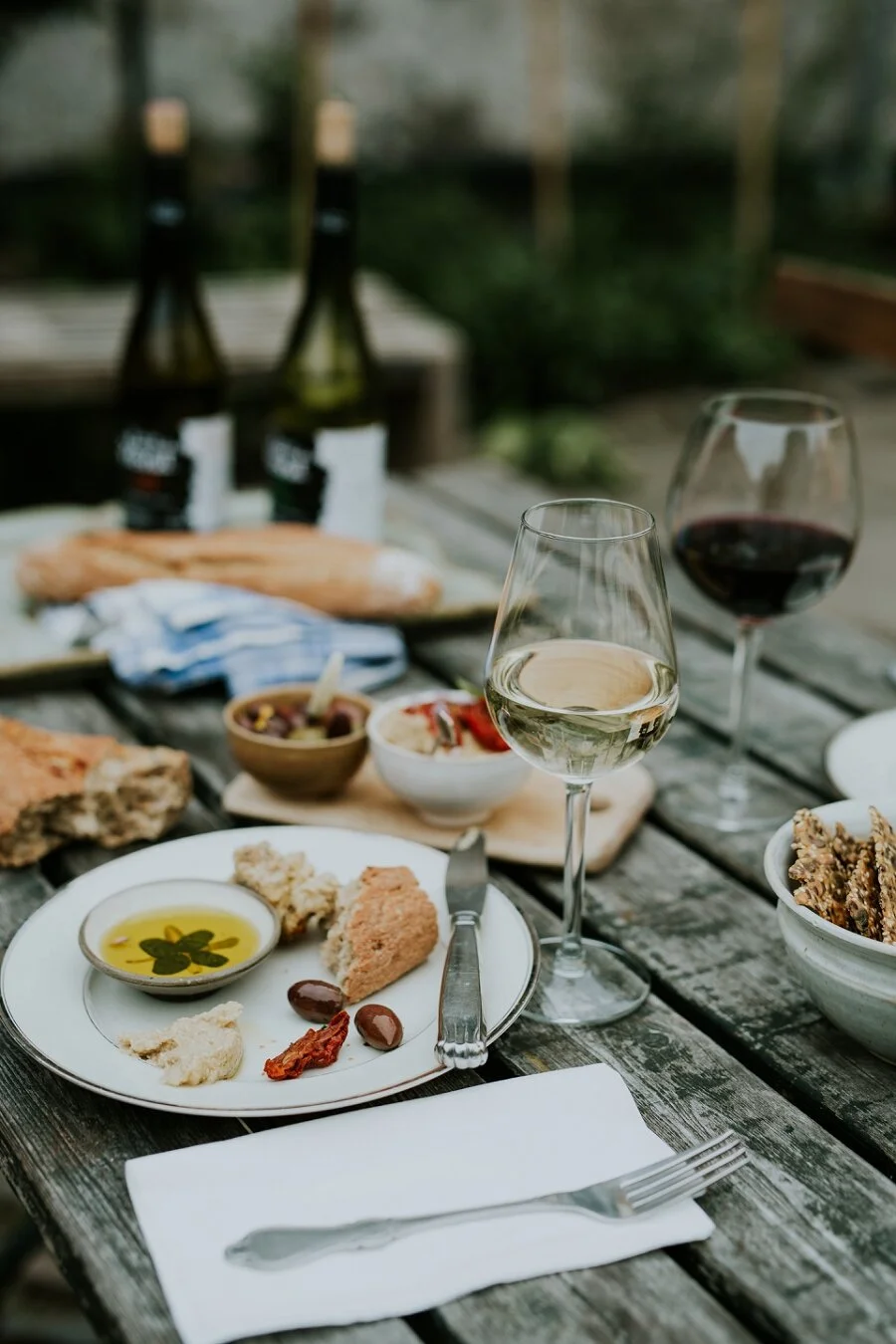 An outdoor lunch at Den Gamle Kobmandsgaard in Aeroeskoebing, featuring fresh bread, bowls of tapas, craft beer, and glasses of wine in the cozy courtyard garden. Ideal inspiration for couples eloping on Aeroe Island in Denmark.
