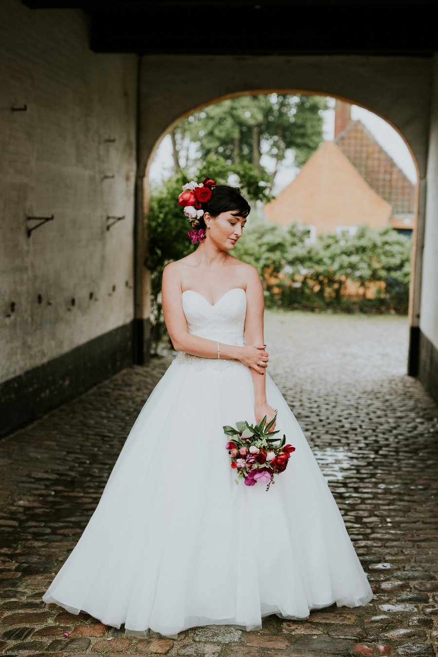 bride in strapless gown holding red and pink floral wedding bouquet  | Aero Island | Danish Island Weddings | Full service Denmark wedding planners