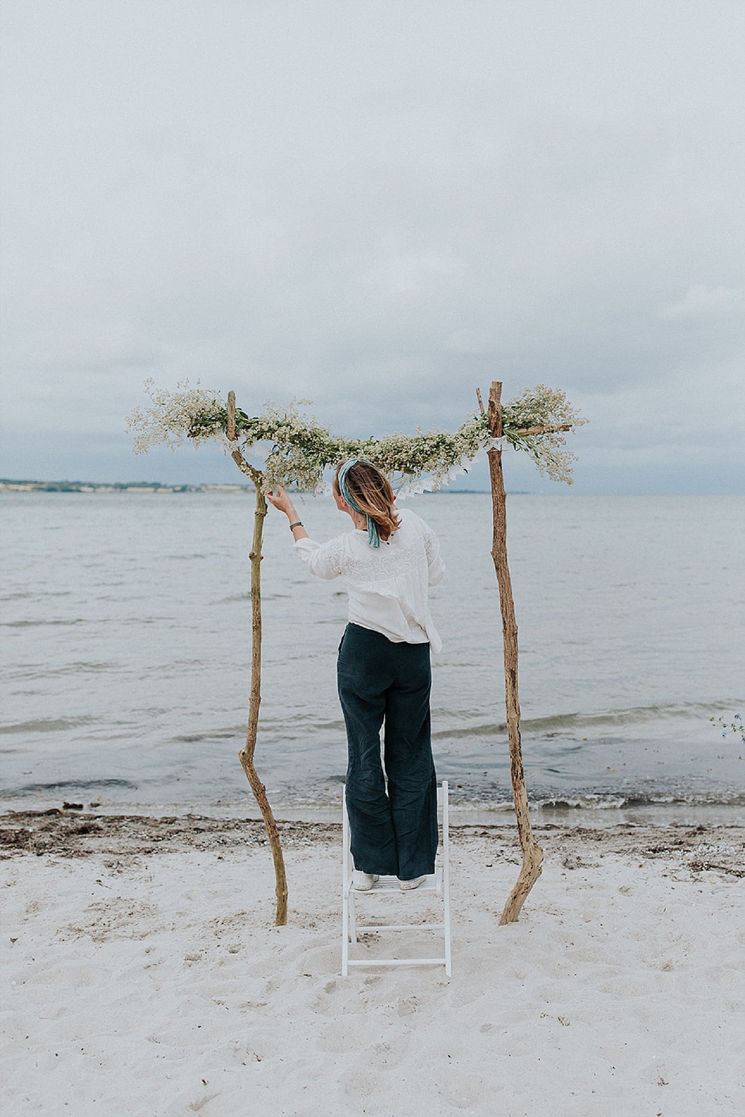 florist arranging greenery on beach wedding trellis arch | Danish Island Weddings | Full service Denmark wedding planners