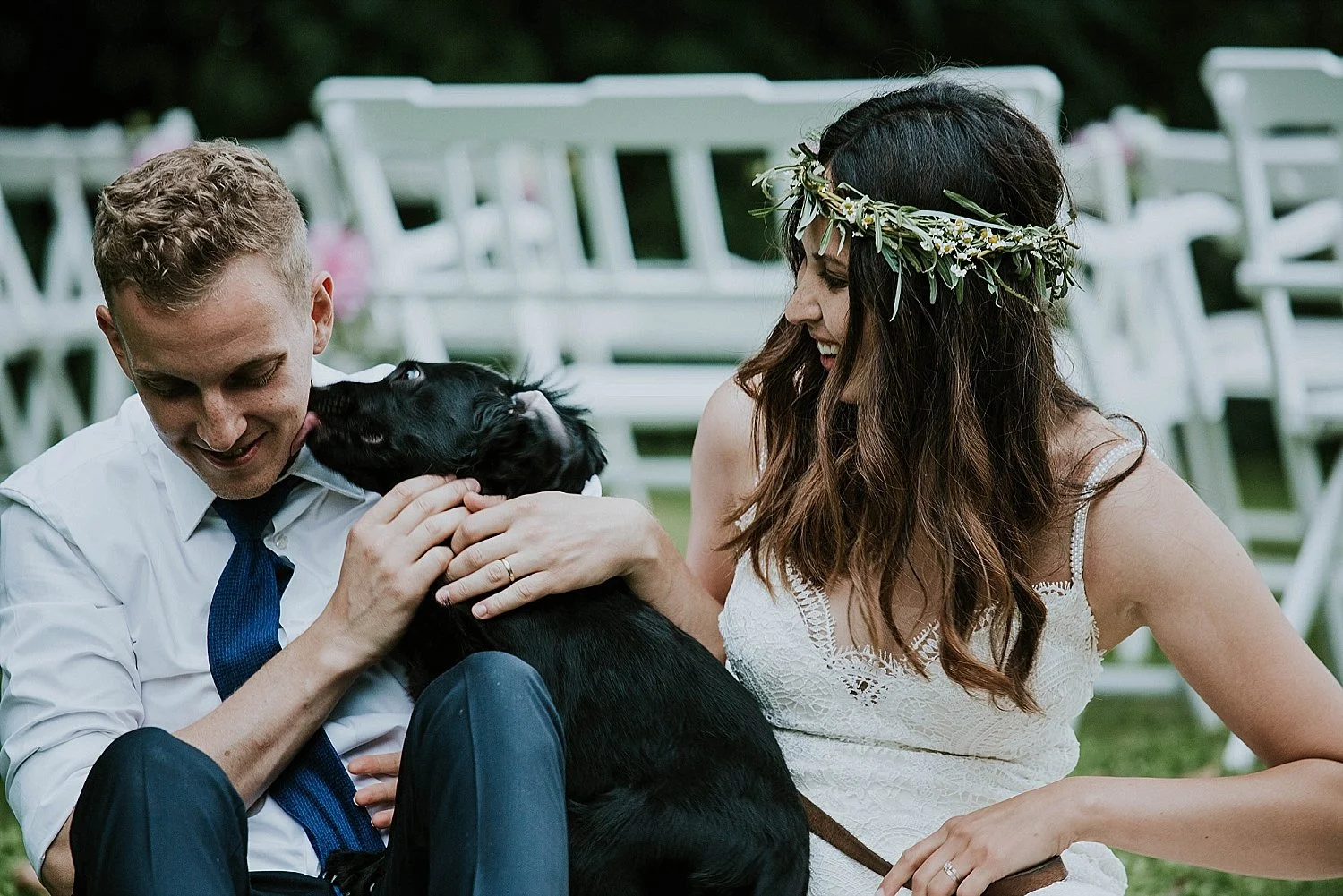 Happy international couple before their wedding in Denmark, with a black puppy licking the groom's face.