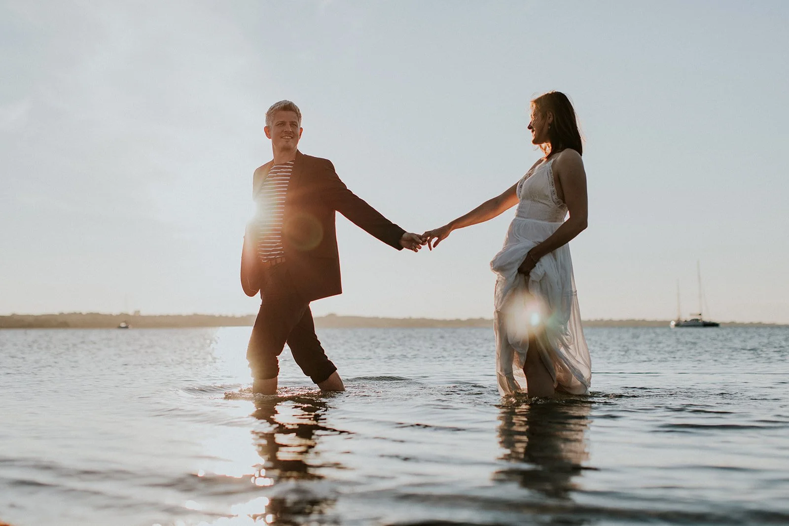 A bride and groom holding hands and walking barefoot in the water during a romantic beach wedding sunset in Denmark