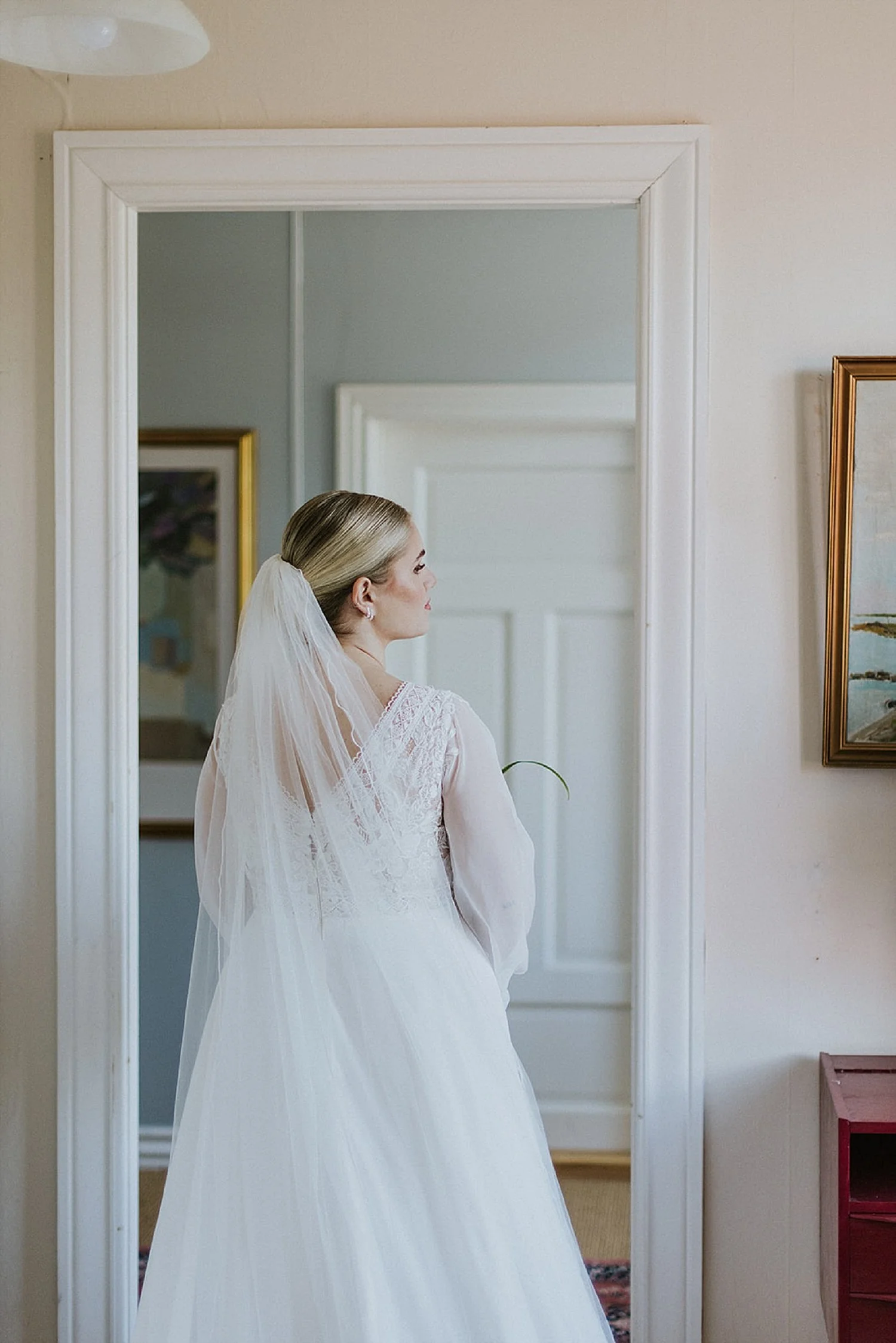 Full length back view of a blonde bride with a sleek bridal updo and wedding veil at The Old Merchants House in Aeroeskobing before her ceremony